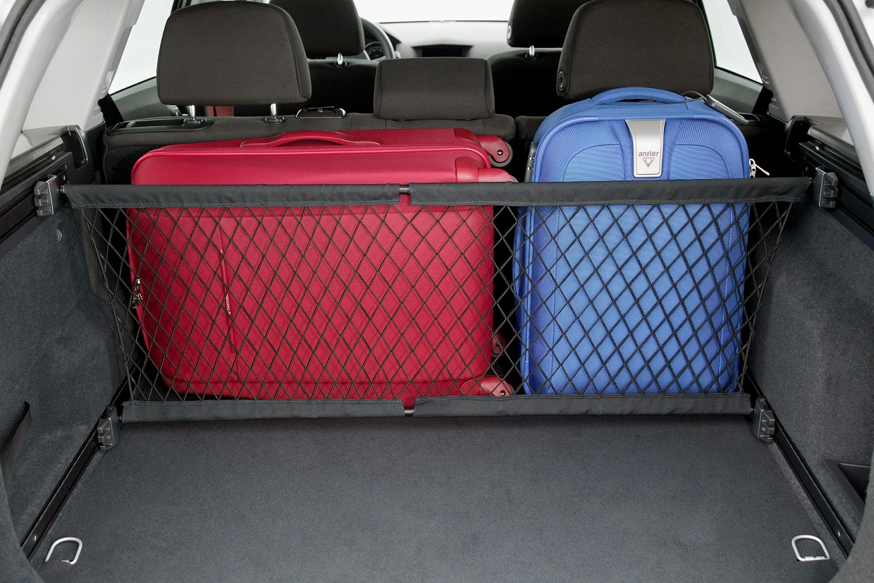 Zwei Koffer, ein roter und ein blauer, stehen im Kofferraum eines Autos, gesichert durch ein Netz.