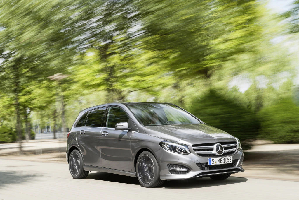 Silberner Mercedes-Benz fährt zügig auf einer von Bäumen gesäumten Straße. Dynamische Aufnahme mit Bewegungsunschärfe.
