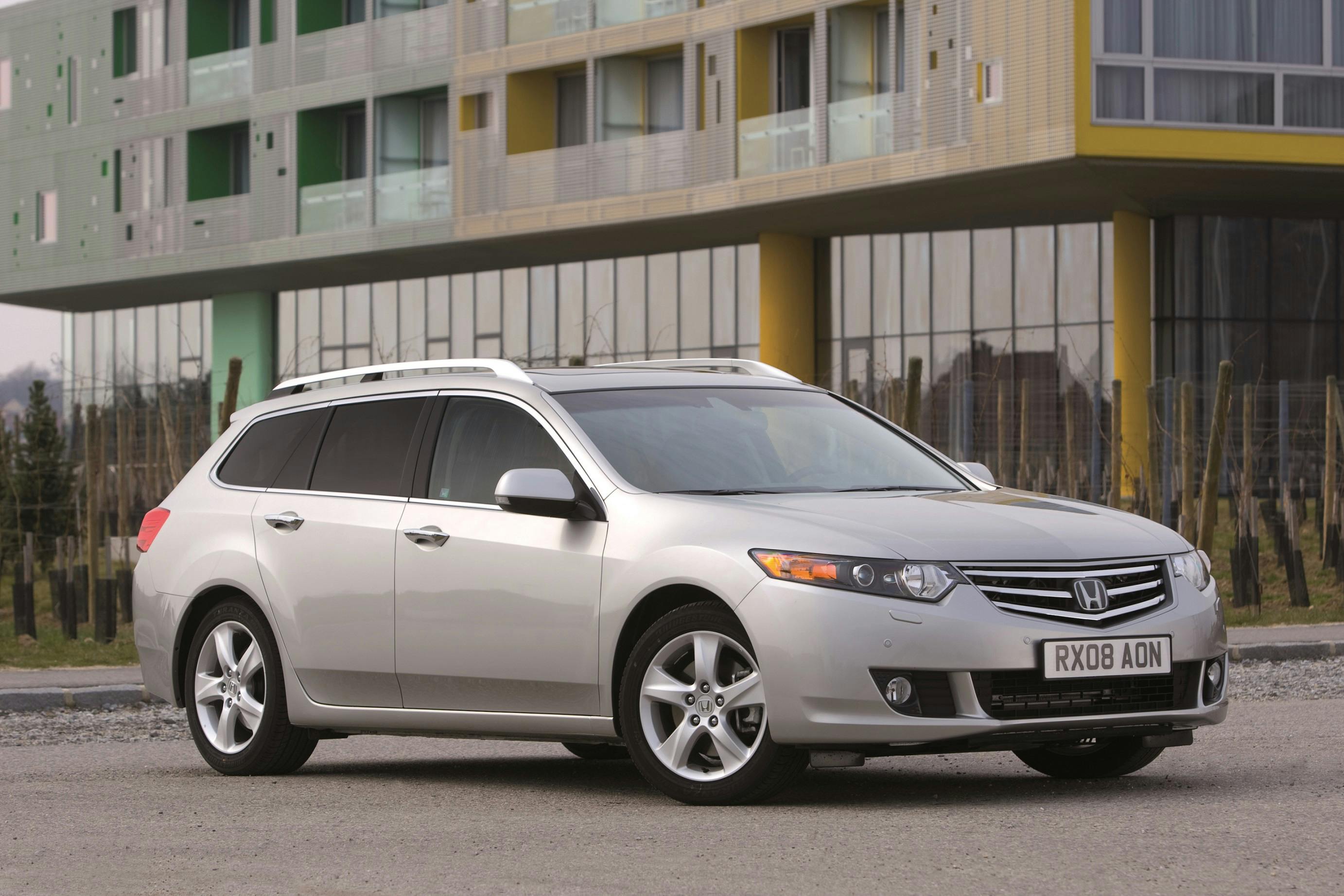 Silberner Kombi-Pkw parkt vor einem modernen Gebäude mit bunten Balkonen.