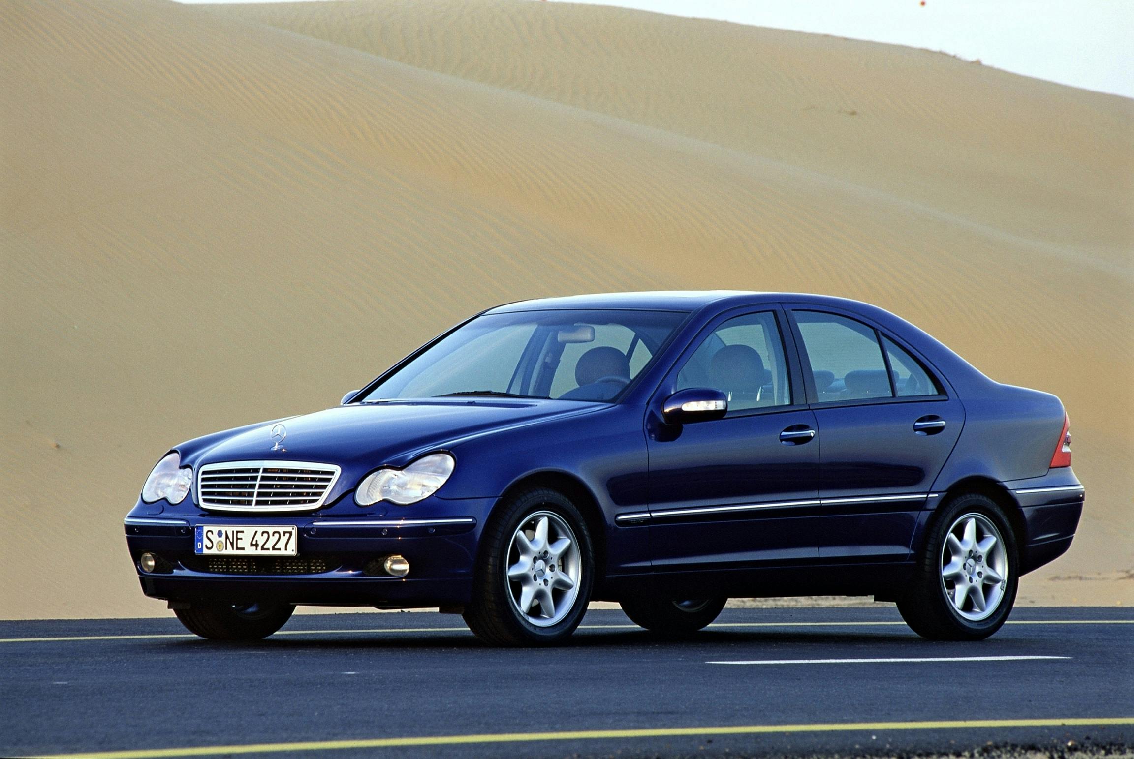 Blauer Mercedes-Benz C-Klasse Limousine auf einer asphaltierten Straße, umgeben von Sanddünen in einer Wüstenlandschaft.