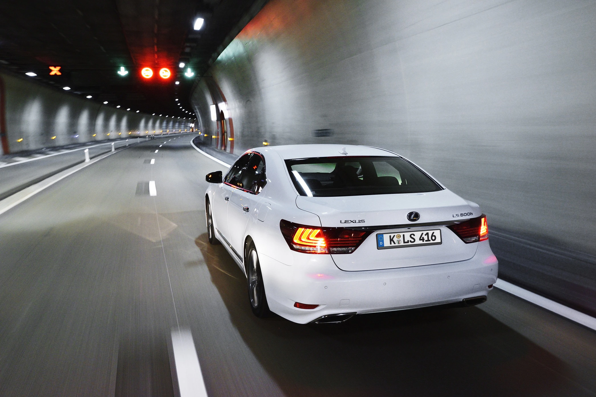Weißes Auto fährt durch beleuchteten Autobahntunnel. Rückansicht, dynamische Bewegung, grüne und rote Lichter sichtbar vorne.