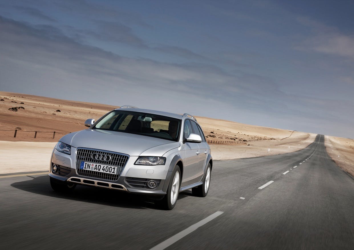 Silbernes Auto fährt auf einer Straße durch eine Wüstenlandschaft unter blauem Himmel.