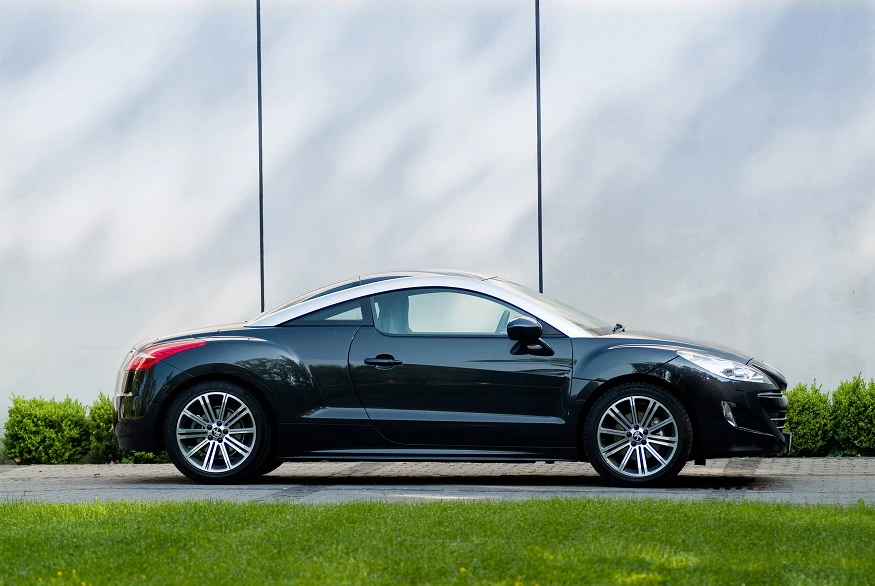 Schwarzes Sportcoupé parkend vor einer grauen Wand und grünem Rasen im Vordergrund. Elegantes, schnittiges Design mit silbernen Felgen.
