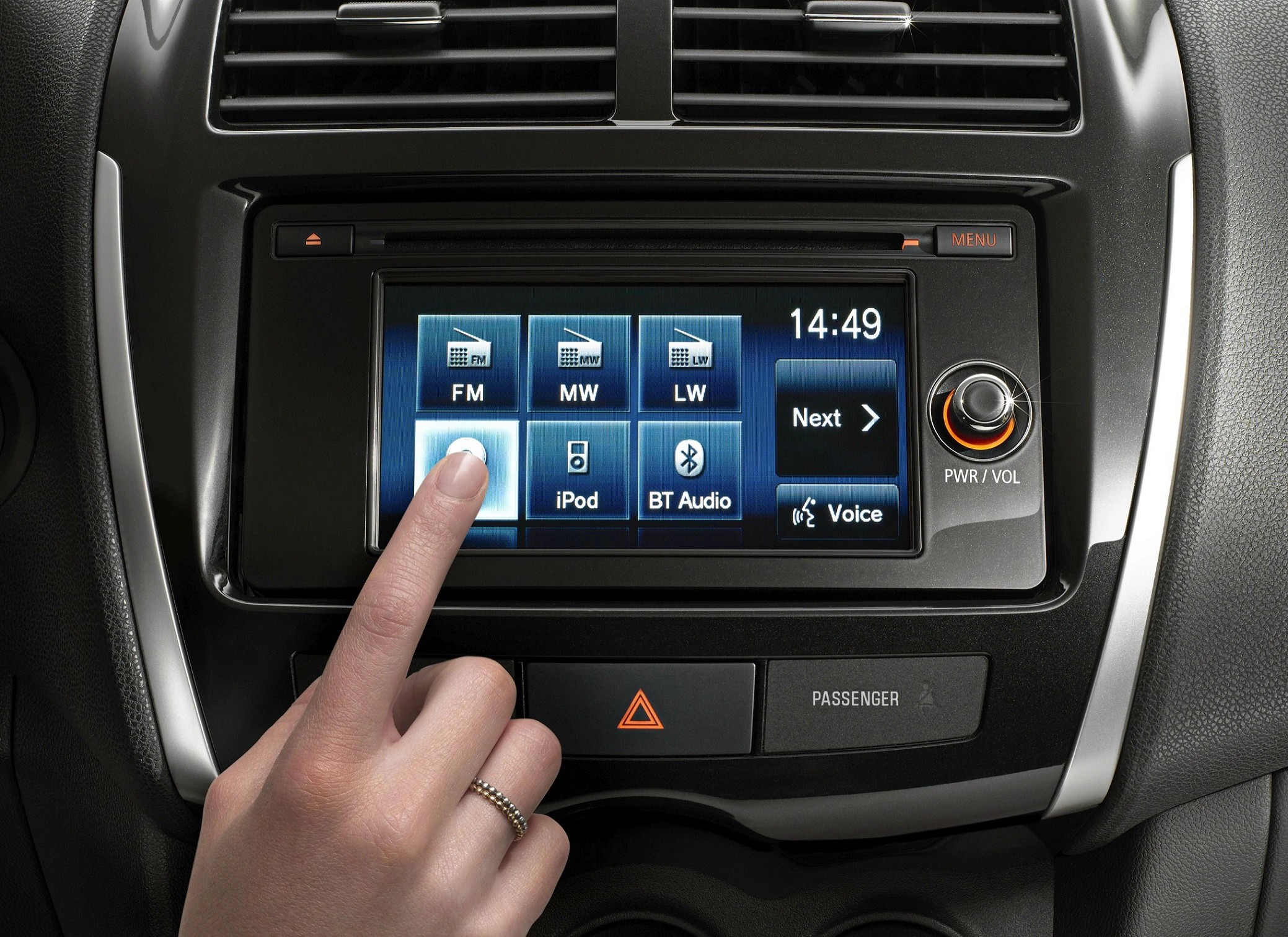 Nahaufnahme eines Autoradios mit Touchscreen. Eine Hand tippt auf das Display, das verschiedene Audio-Optionen und die Uhrzeit 14:49 zeigt.