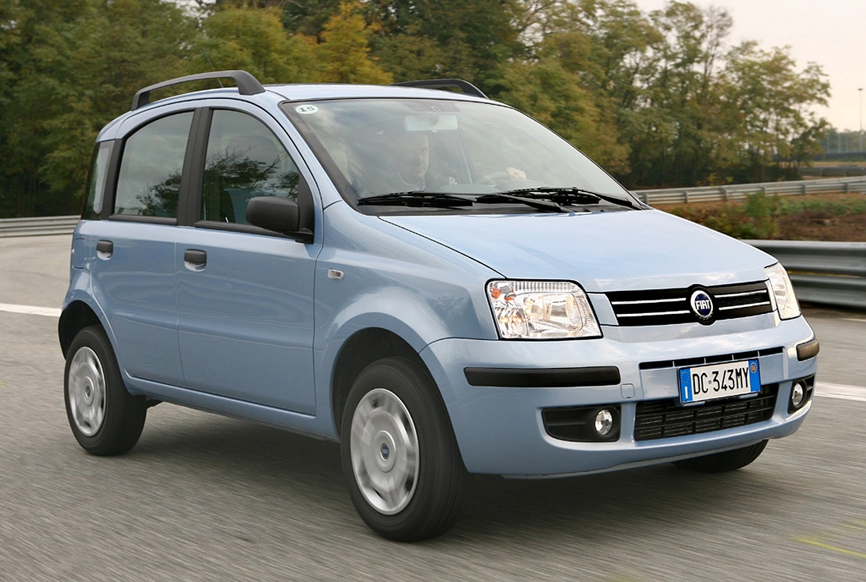 Ein blauer Fiat Panda fährt auf einer Landstraße. Im Hintergrund sind Bäume und ein bewölkter Himmel zu sehen.