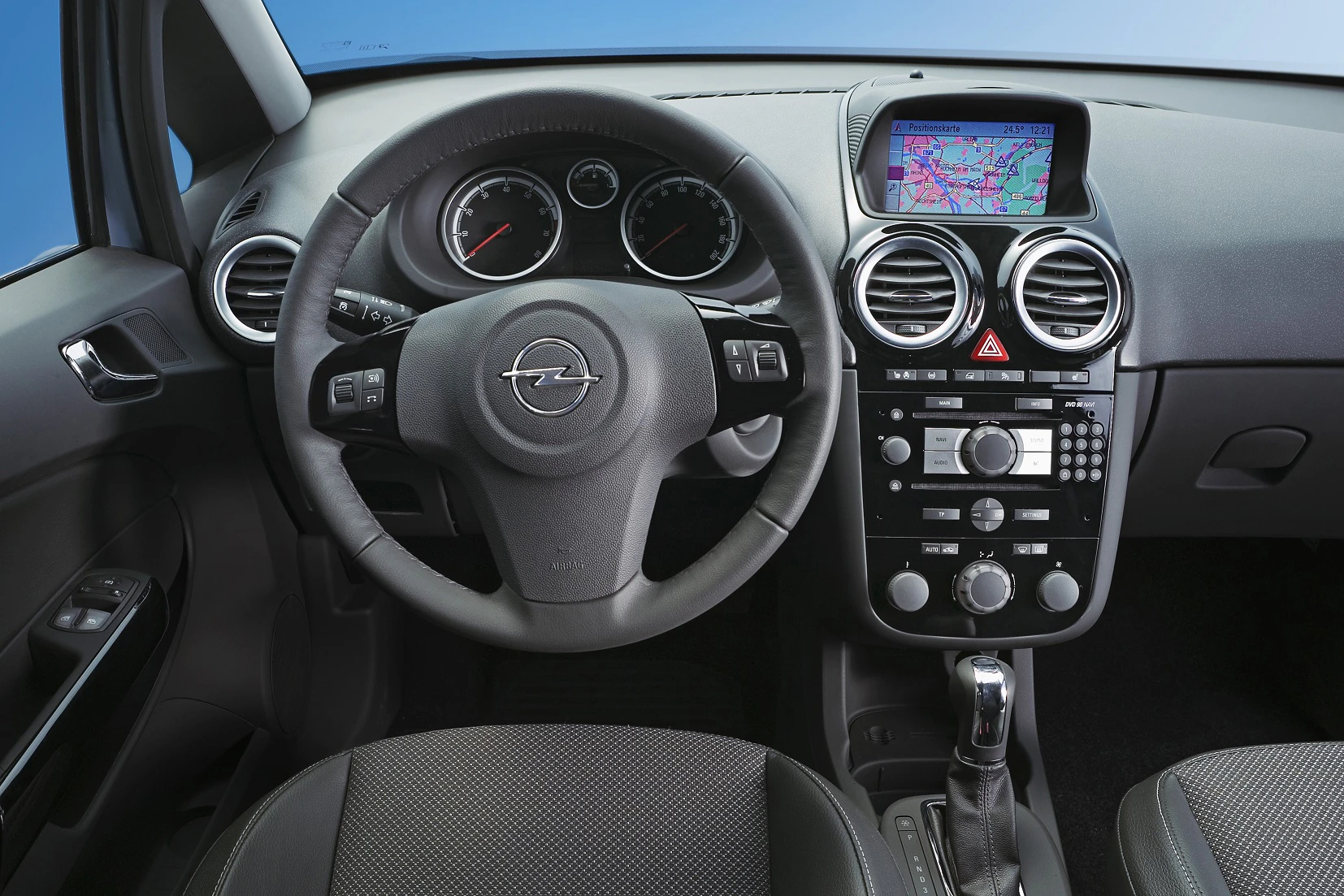 Innenraum eines Autos mit Lenkrad und Dashboard. Auf dem Bildschirm ist ein Navigationssystem zu sehen. Klimaregler und Radio darunter.