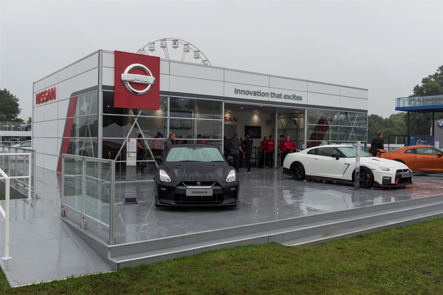 Nissan-Pavillon mit zwei Sportwagen, einem schwarzen und einem weißen, auf einer Motorshow. Im Hintergrund Besucher und ein Riesenrad.