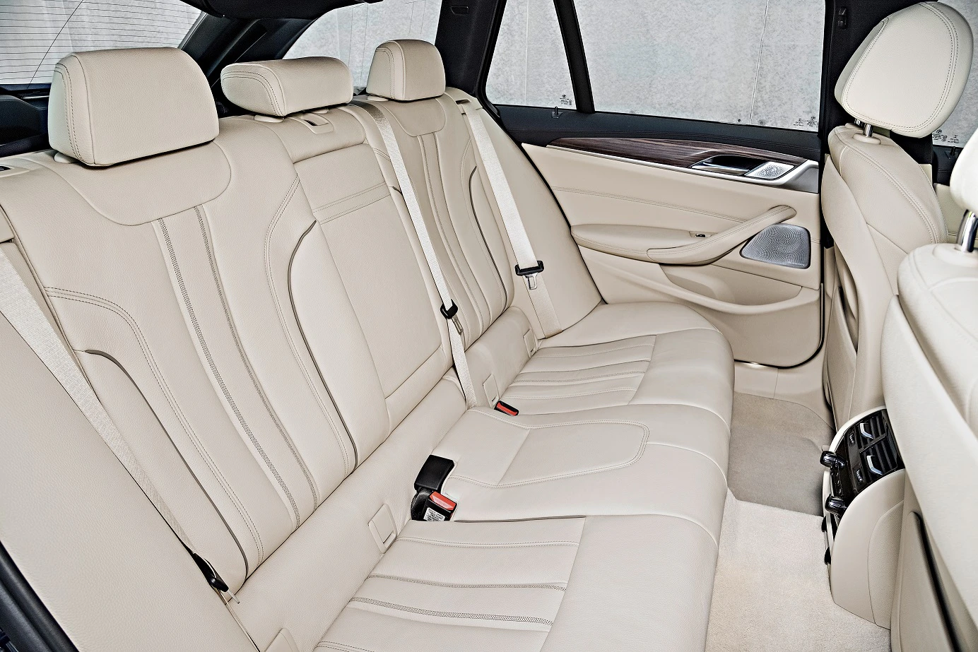 Rückansicht eines Autos mit beigen Ledersitzen, die Sitzbank hat drei Plätze. Die Innenausstattung wirkt luxuriös und modern.