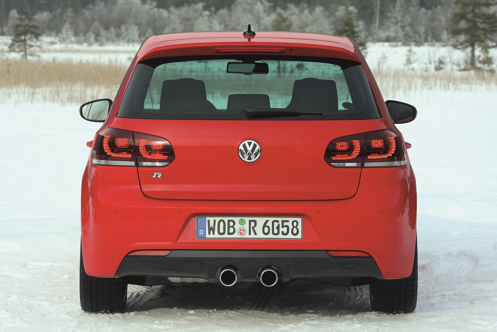 Roter Volkswagen Golf R auf schneebedecktem Boden, von hinten fotografiert, mit sichtbarem Auspuff und Nummernschild.