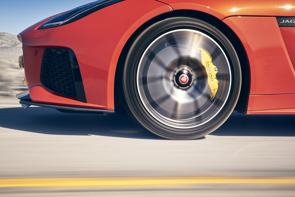 Nahaufnahme eines fahrenden, roten Sportwagens mit sichtbarer Bewegung der Felge und gelbem Bremssattel.