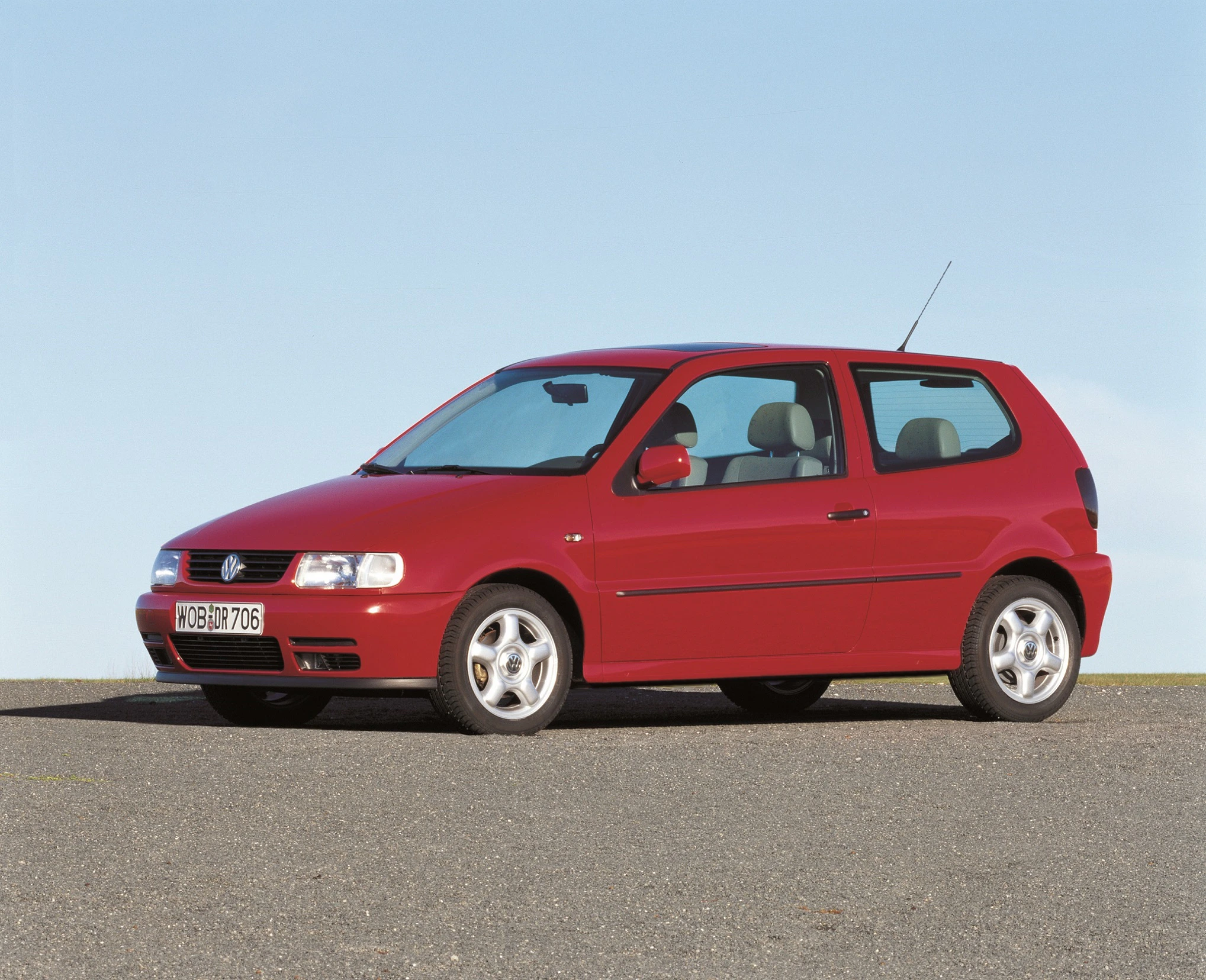 Roter, dreitüriger Volkswagen Polo auf Asphalt vor blauem Himmel, frontal seitlich fotografiert.