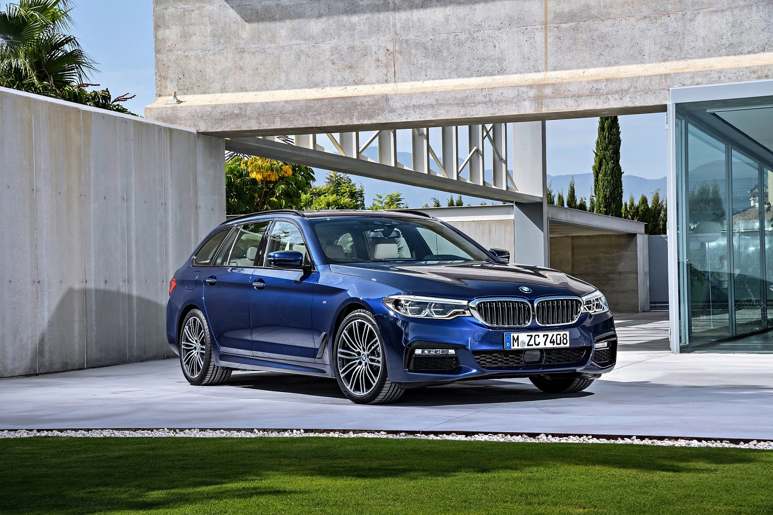 Blaues BMW Kombi-Auto steht auf einer modernen Einfahrt vor einem architektonischen Gebäude mit klarer Linienführung.