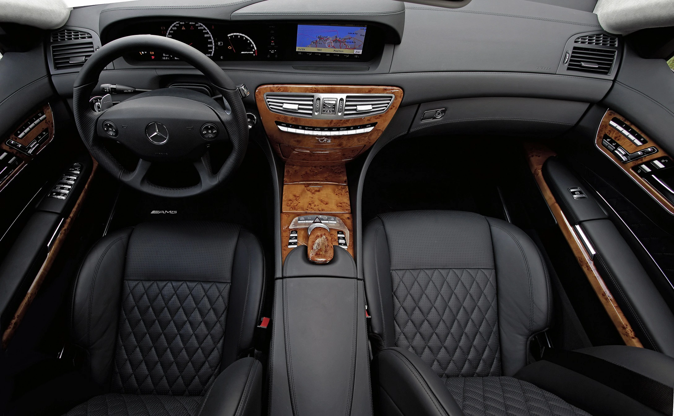 Innenraum eines Mercedes mit schwarzer Lederpolsterung, Holzakzenten, Lenkrad und digitalem Display. Luxuriöses und elegantes Design.
