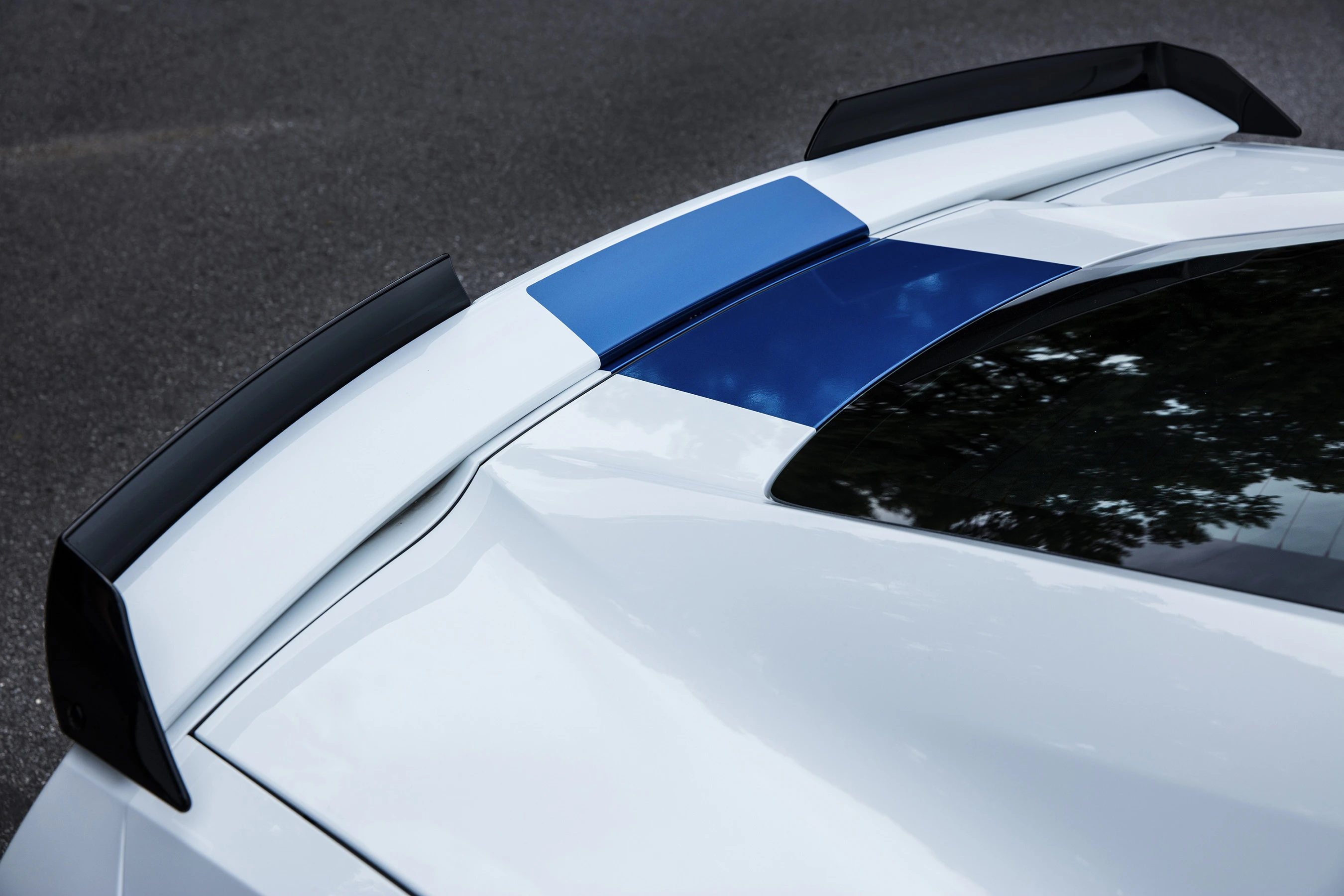 Weißes Auto mit blauem Streifen auf dem Dach und schwarzem Spoiler, von oben fotografiert.