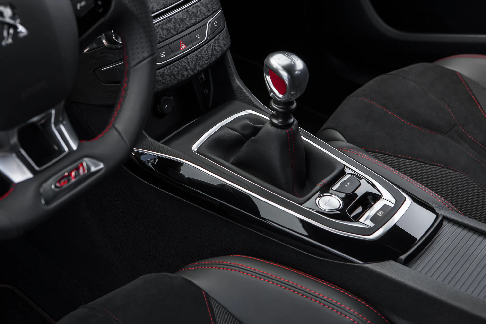 Nahaufnahme eines Auto-Innenraums mit einem manuellen Schalthebel, Lenkrad und schwarzen Sitzen mit roten Nähten.