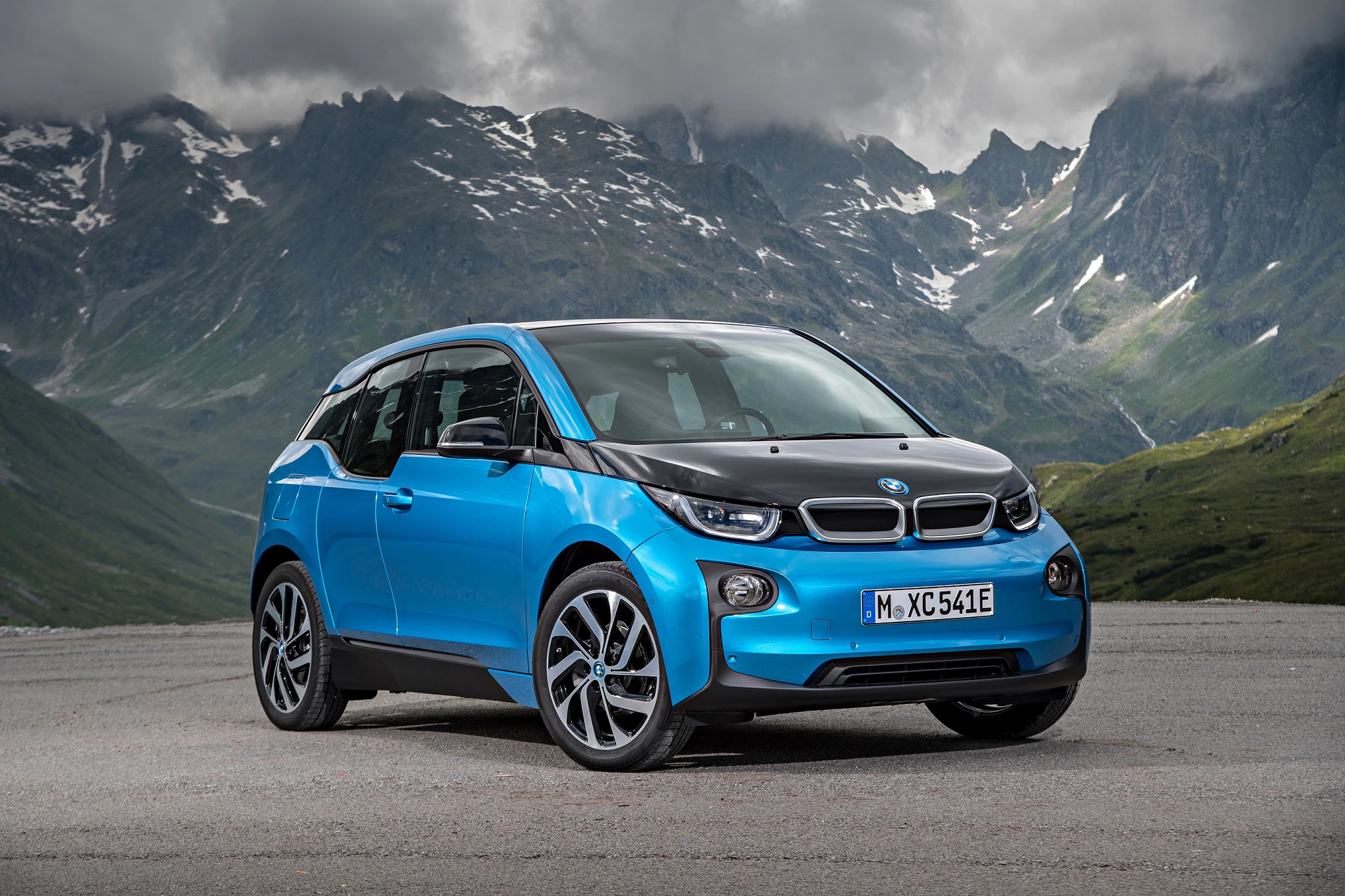 Blauer BMW i3 parkt vor einer beeindruckenden Bergkulisse mit bewölktem Himmel.