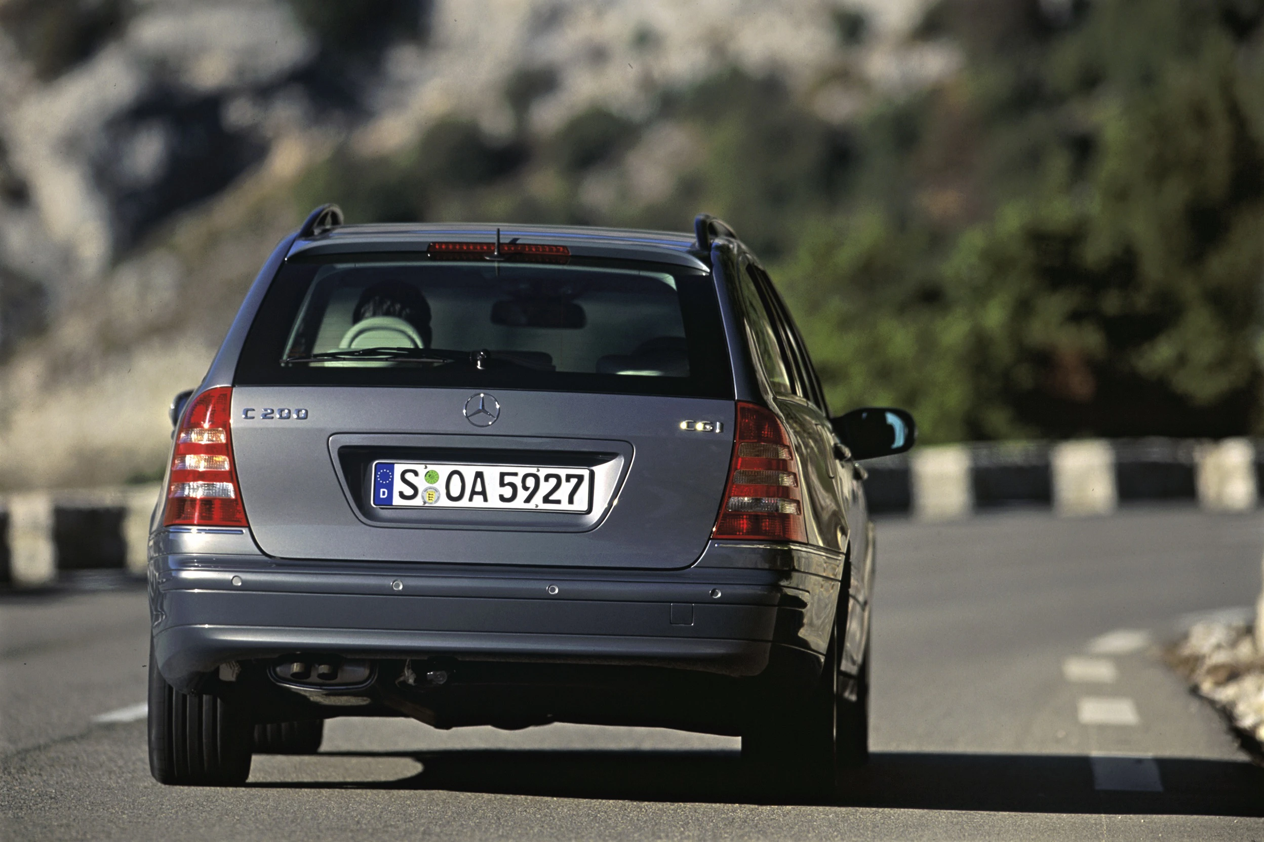Silberner Mercedes-Limousine fährt auf einer kurvigen Bergstraße. Das Fahrzeug ist von hinten aufgenommen.