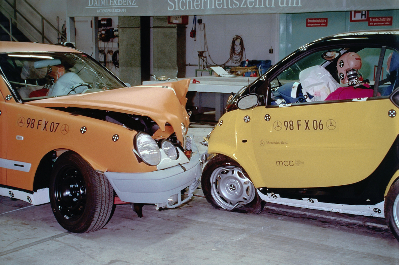 Zwei Autos bei einem Crashtest im Sicherheitszentrum von Mercedes-Benz, mit Dummies als Passagieren und sichtbarer Beschädigung an der Fahrzeugfront.
