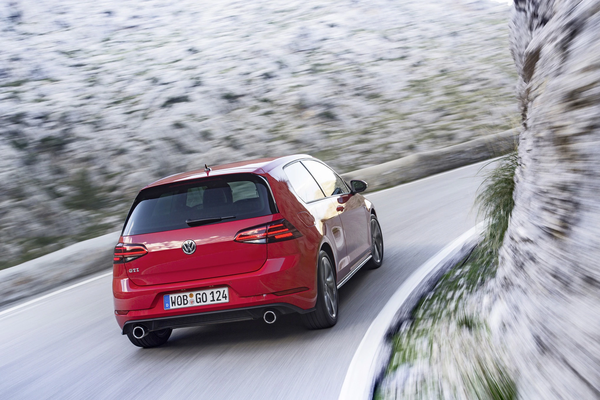 Roter VW Golf GTI fährt auf einer kurvigen Bergstraße entlang einer Felswand, zeigt sportliches Design und Dynamik.
