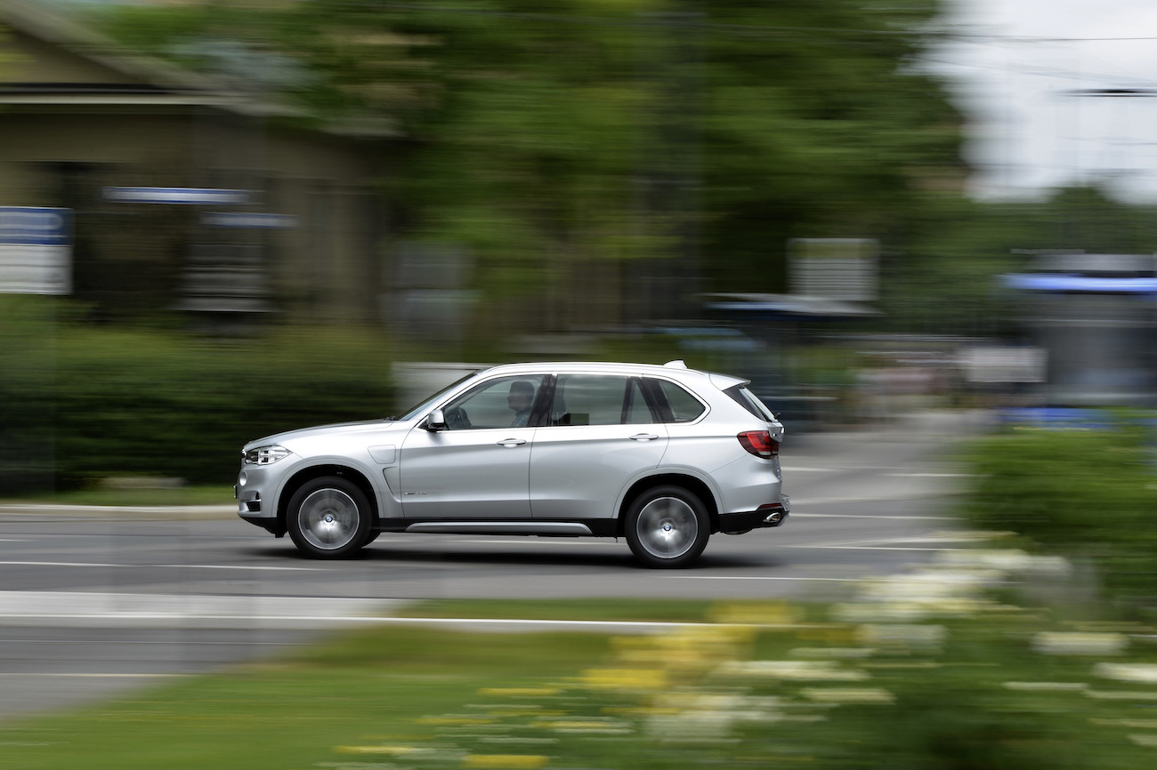 Silberner SUV fährt schnell auf einer Straße, umgeben von grünen Bäumen und unscharfer Umgebung.