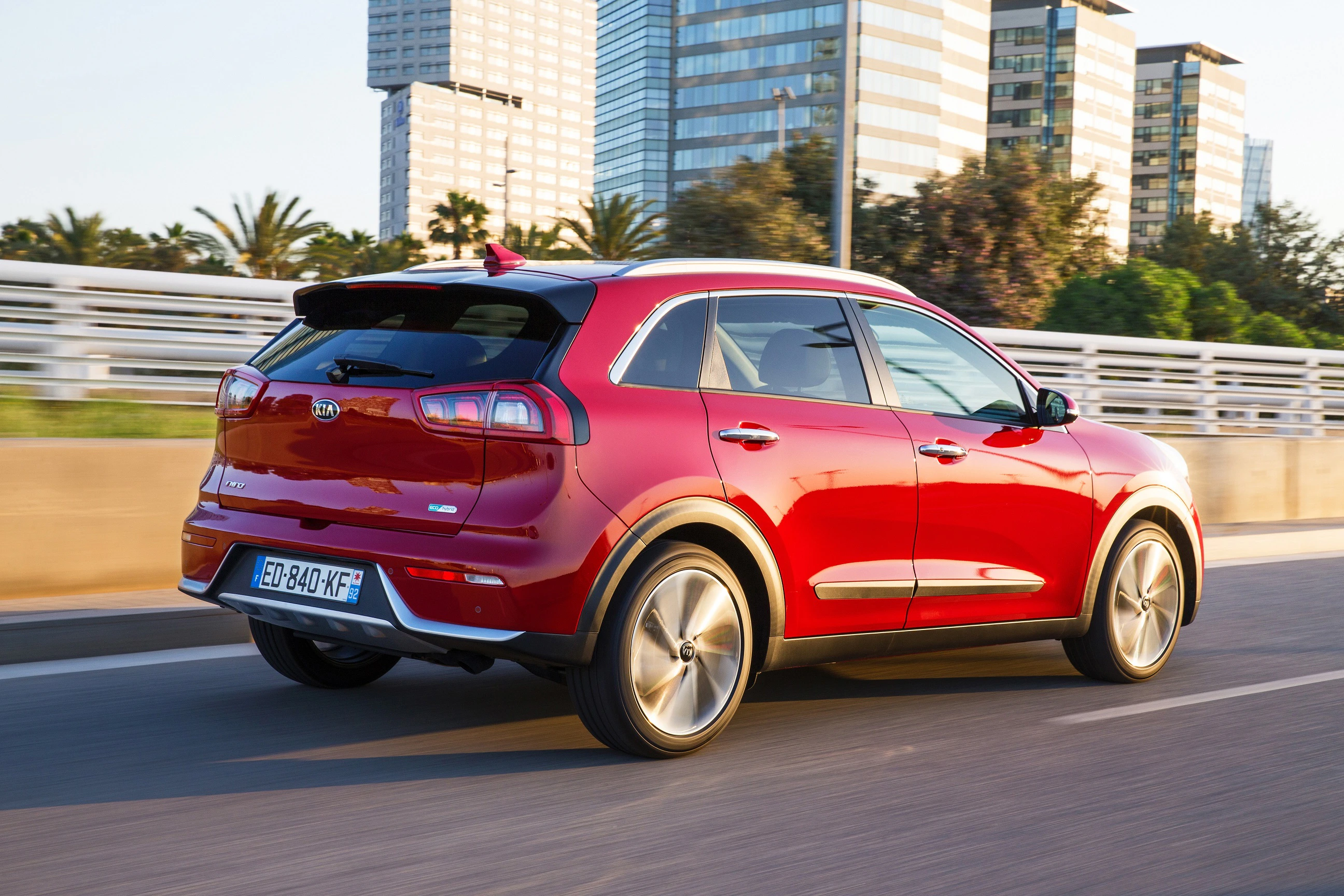 Roter SUV fährt auf einer urbanen Straße, im Hintergrund moderne Gebäude und Palmen.