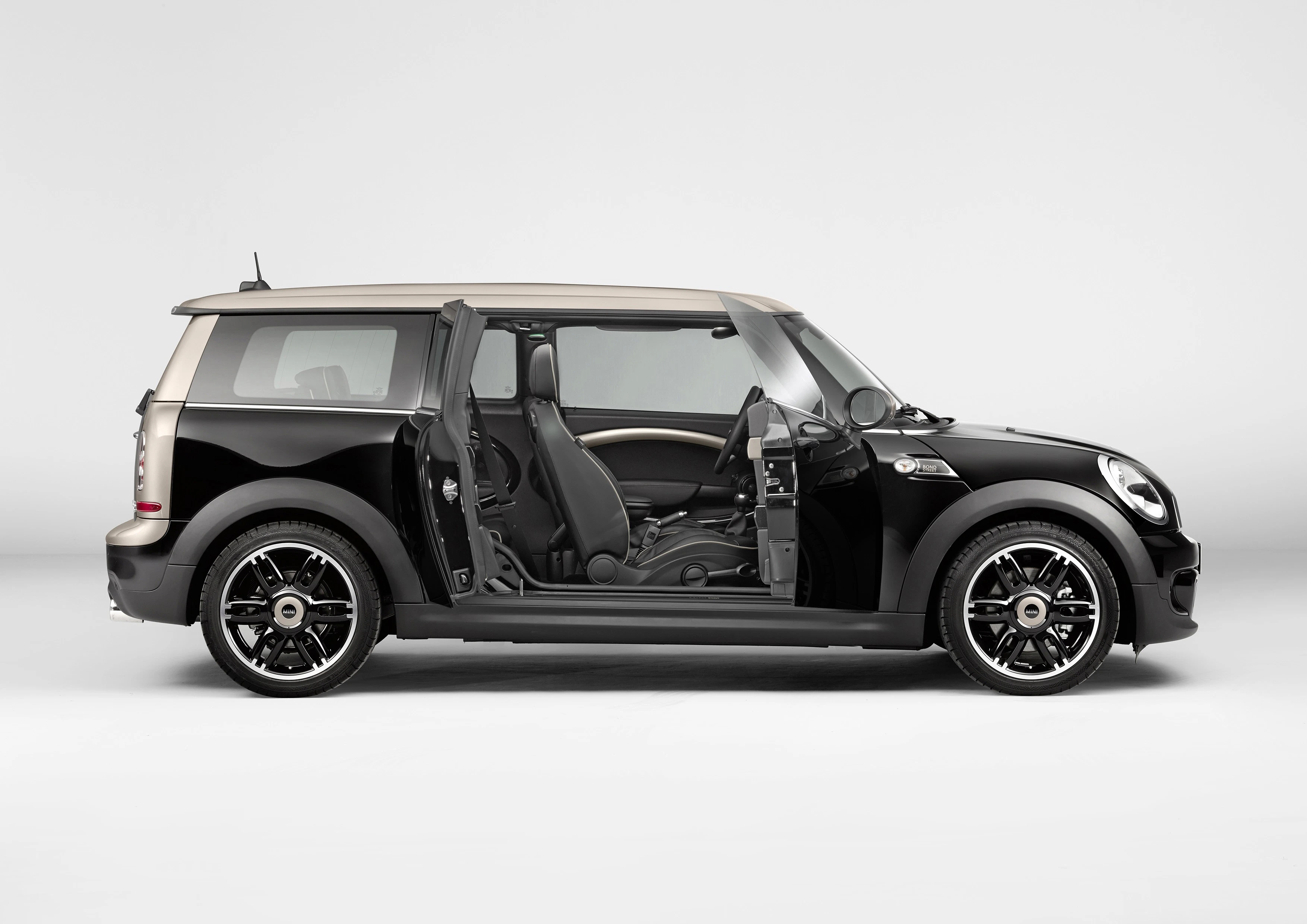Schwarzer Mini Clubman mit geöffneter Seitentür, Seitenansicht, auf grauem Hintergrund.