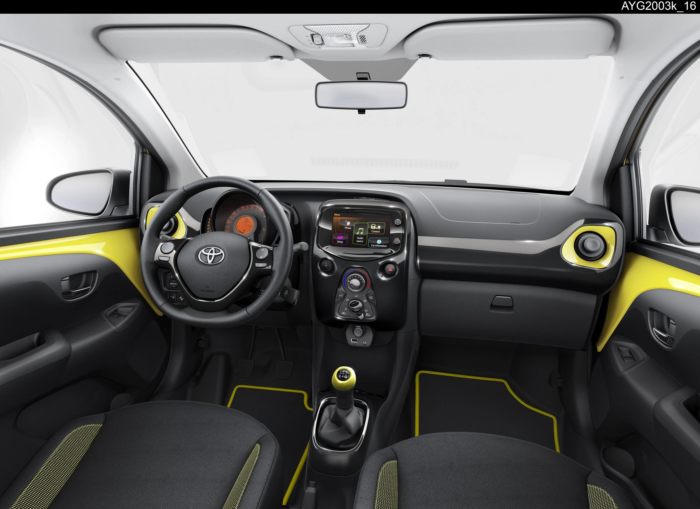 Innenraum eines Autos mit schwarzem Armaturenbrett, gelben Akzenten, Lenkrad mit Toyota-Logo, Touchscreen und manueller Schaltung.