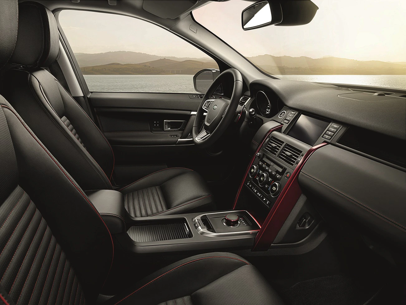 Innenraum eines modernen Autos mit eleganten schwarzen Ledersitzen, rotem Zierstreifen, und Blick auf einen See im Hintergrund.