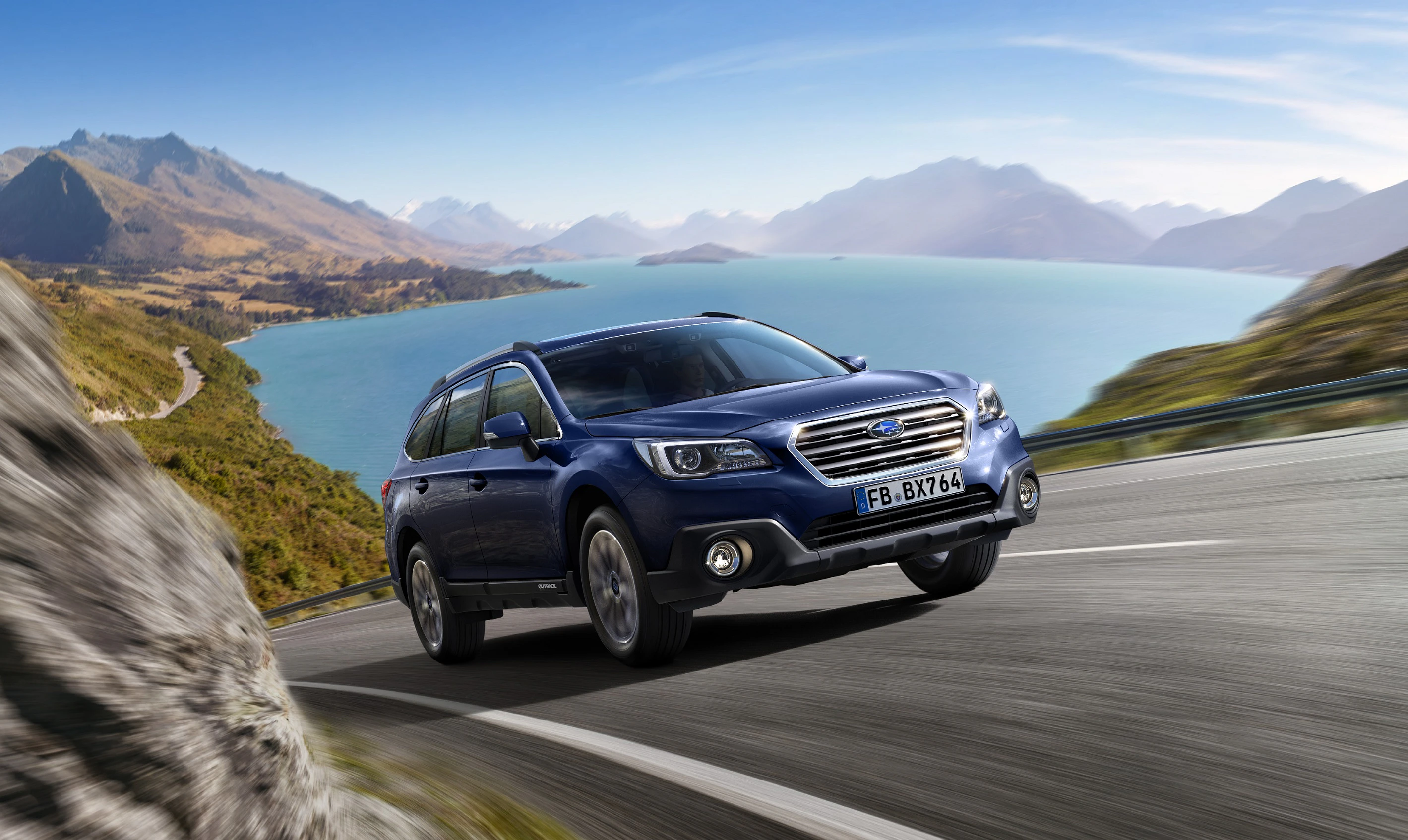 Blauer SUV fährt auf kurviger Bergstraße mit malerischem See und Bergen im Hintergrund unter klarem Himmel.
