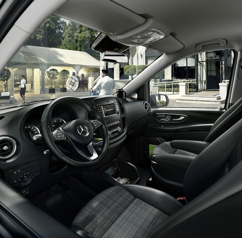 Innenraum eines modernen Mercedes-Fahrzeugs mit lederbezogenen Sitzen und einem hoch entwickelten Armaturenbrett, Blick nach draußen auf Straße.