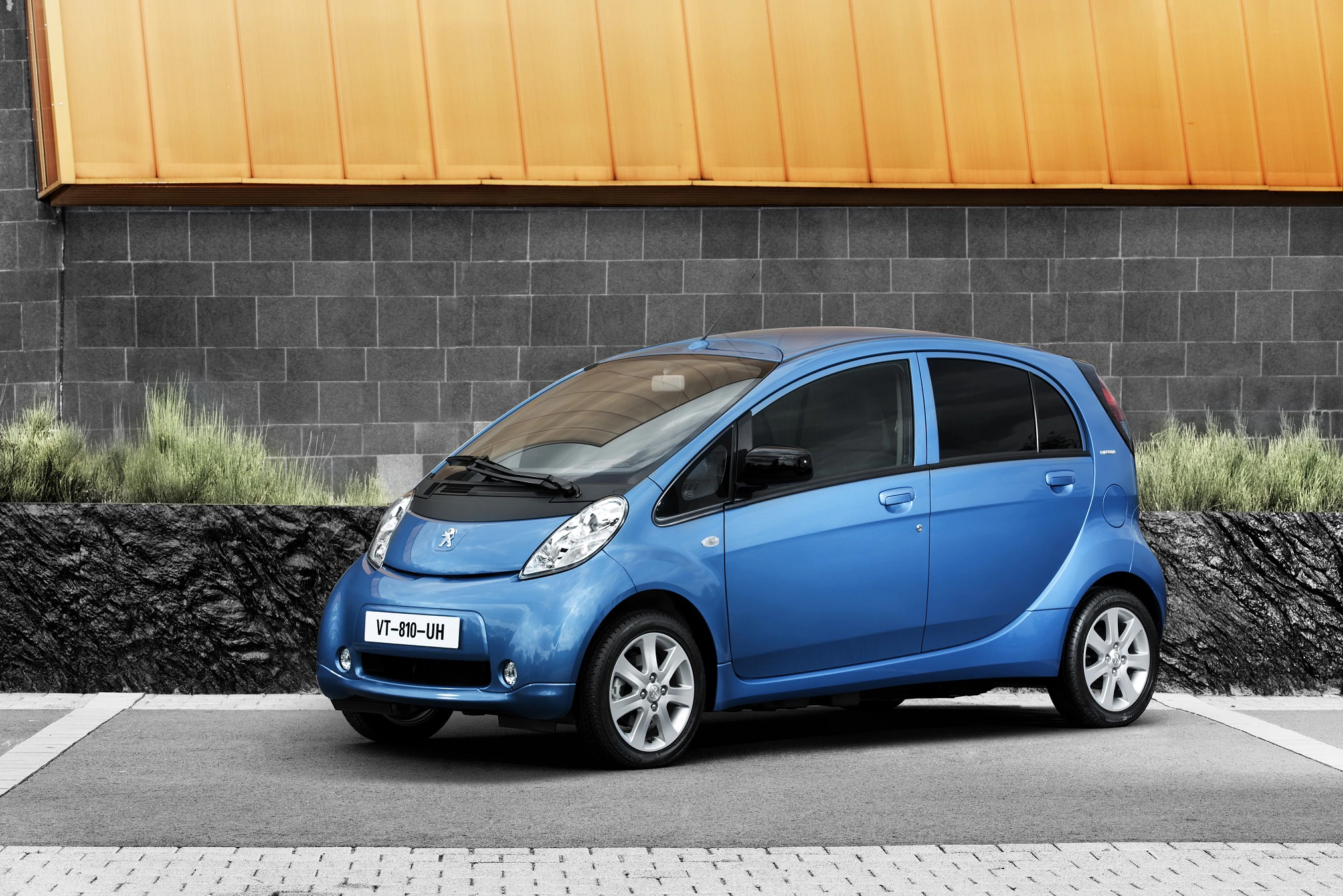 Blaues Kompaktauto parkt vor einer modernen Wand aus schwarzen und orangefarbenen Paneelen.