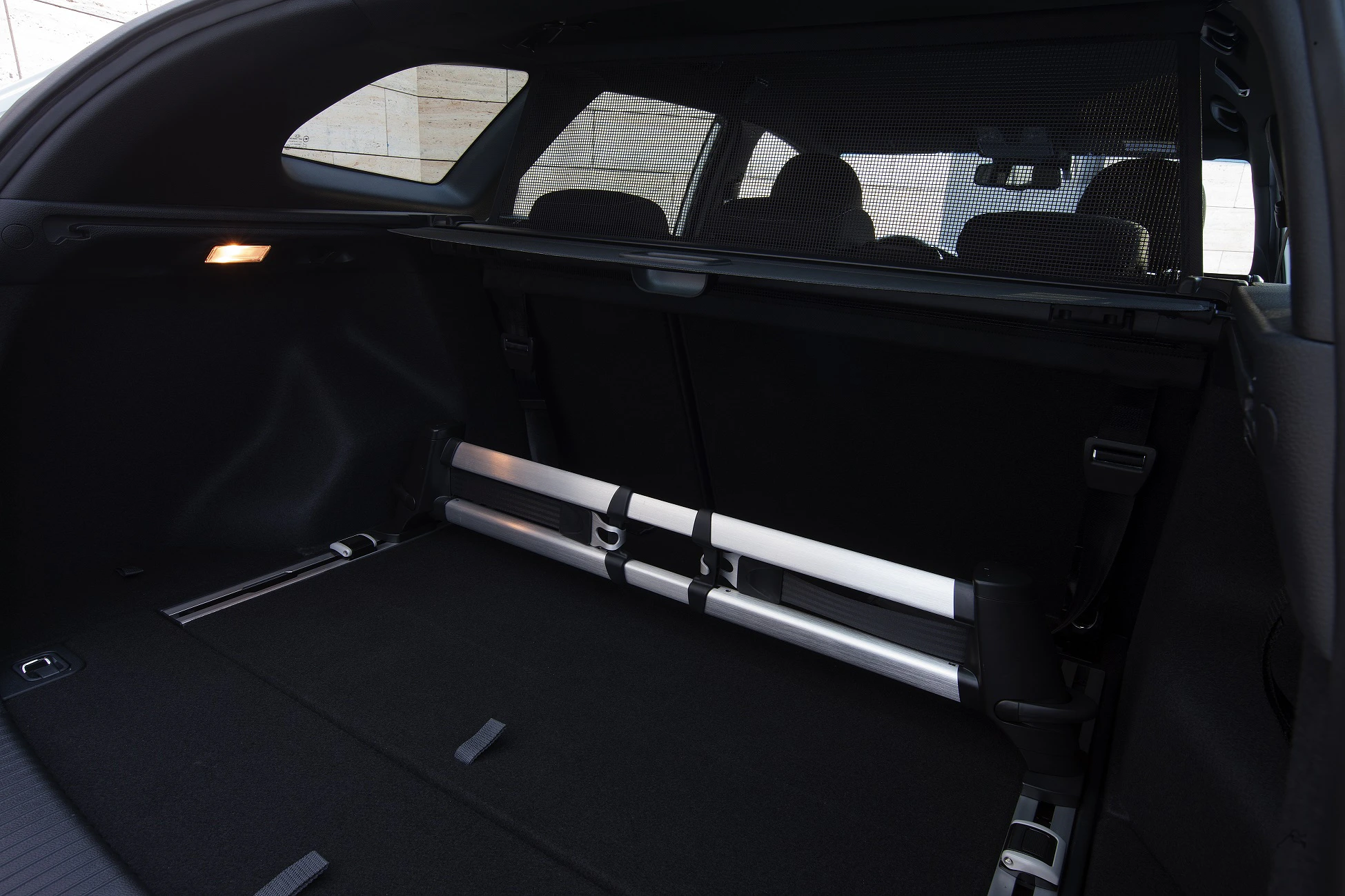 Kofferraum eines Autos mit zusammenklappbaren Sitzen und beleuchtetem Innenraum, schwarz mit Metallakzenten.