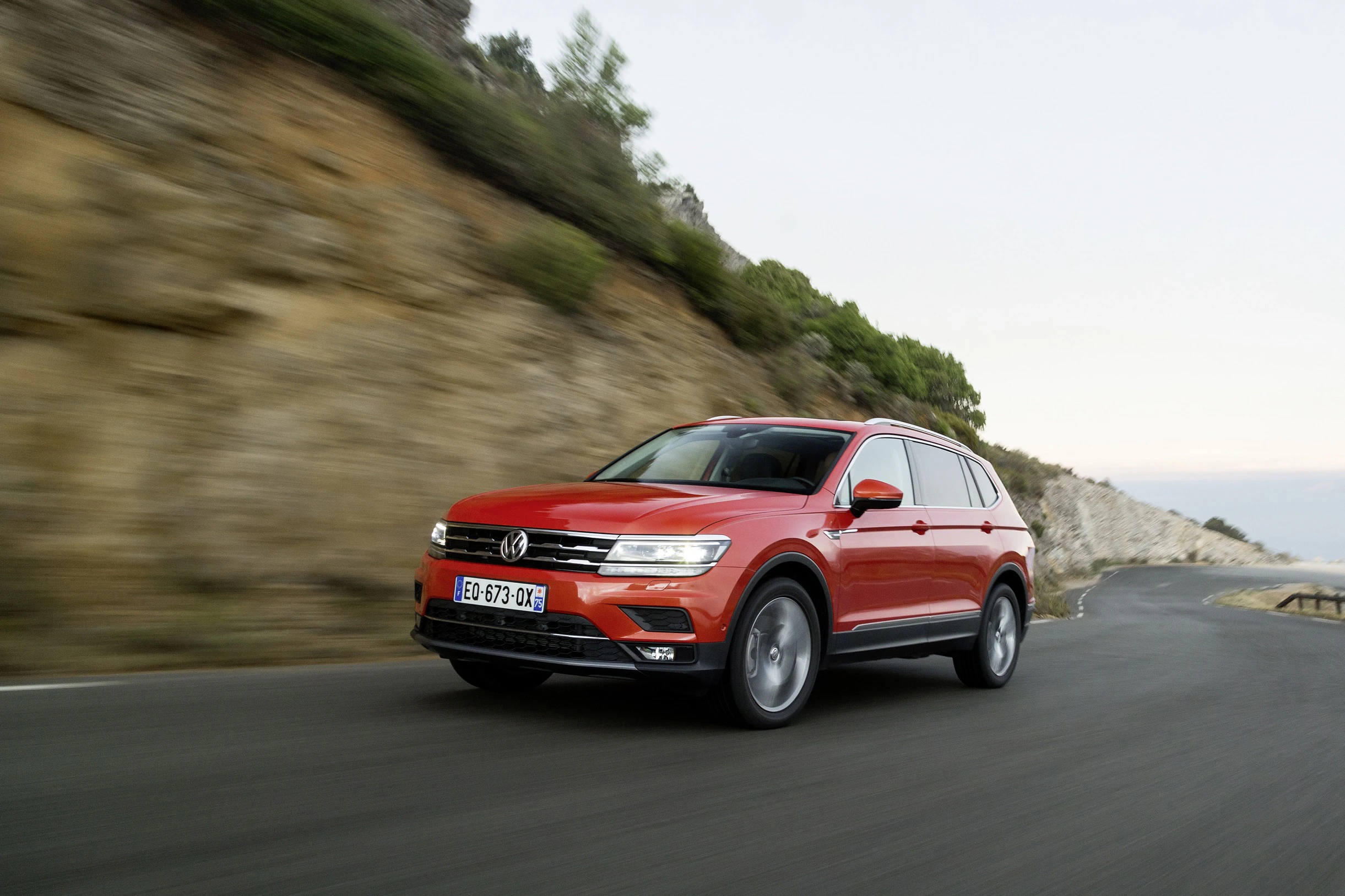 Roter SUV fährt dynamisch auf einer kurvigen Landstraße entlang einer felsigen Landschaft.