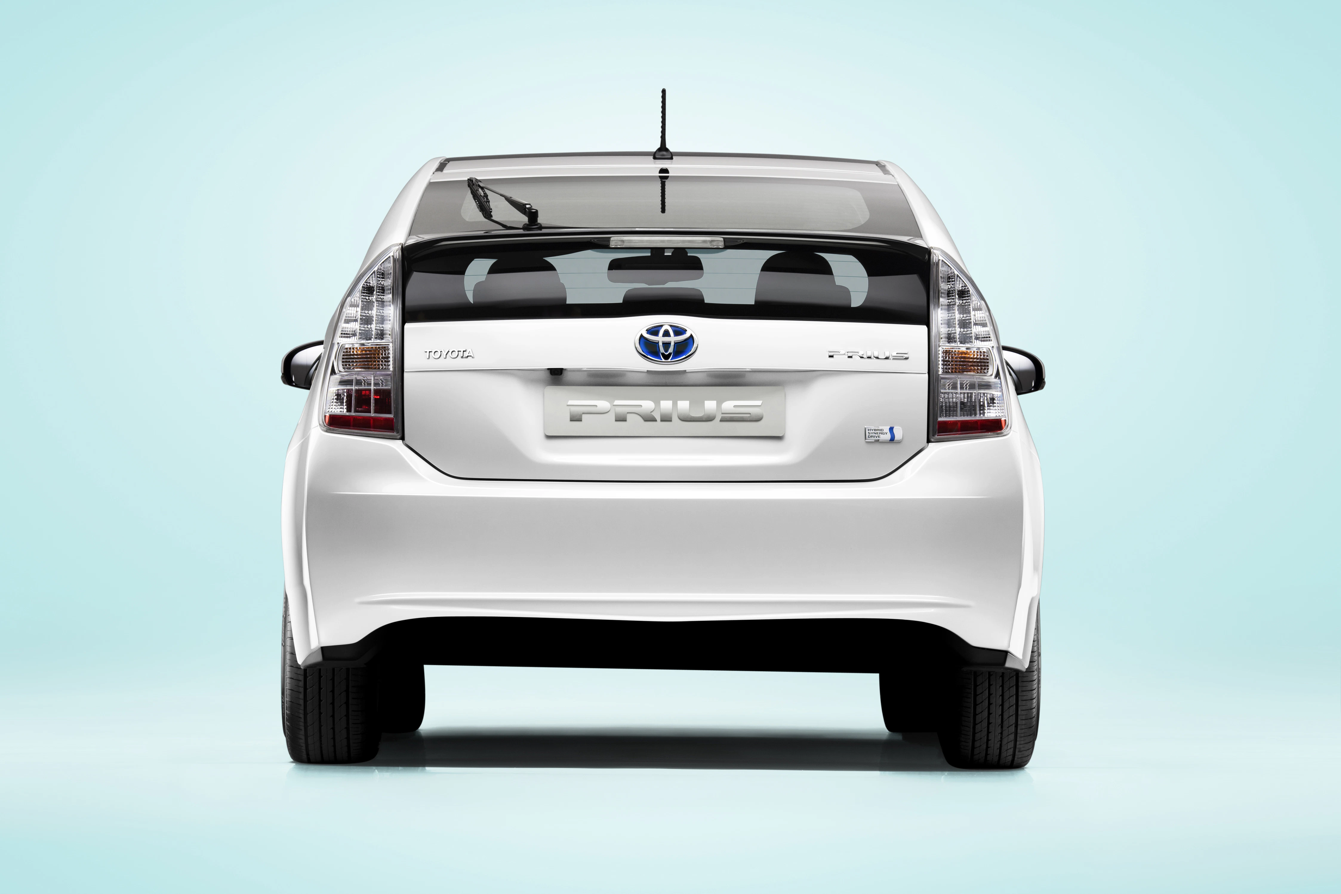 Rückansicht eines weißen Toyota Prius Hybridautos vor einem hellblauen Hintergrund.