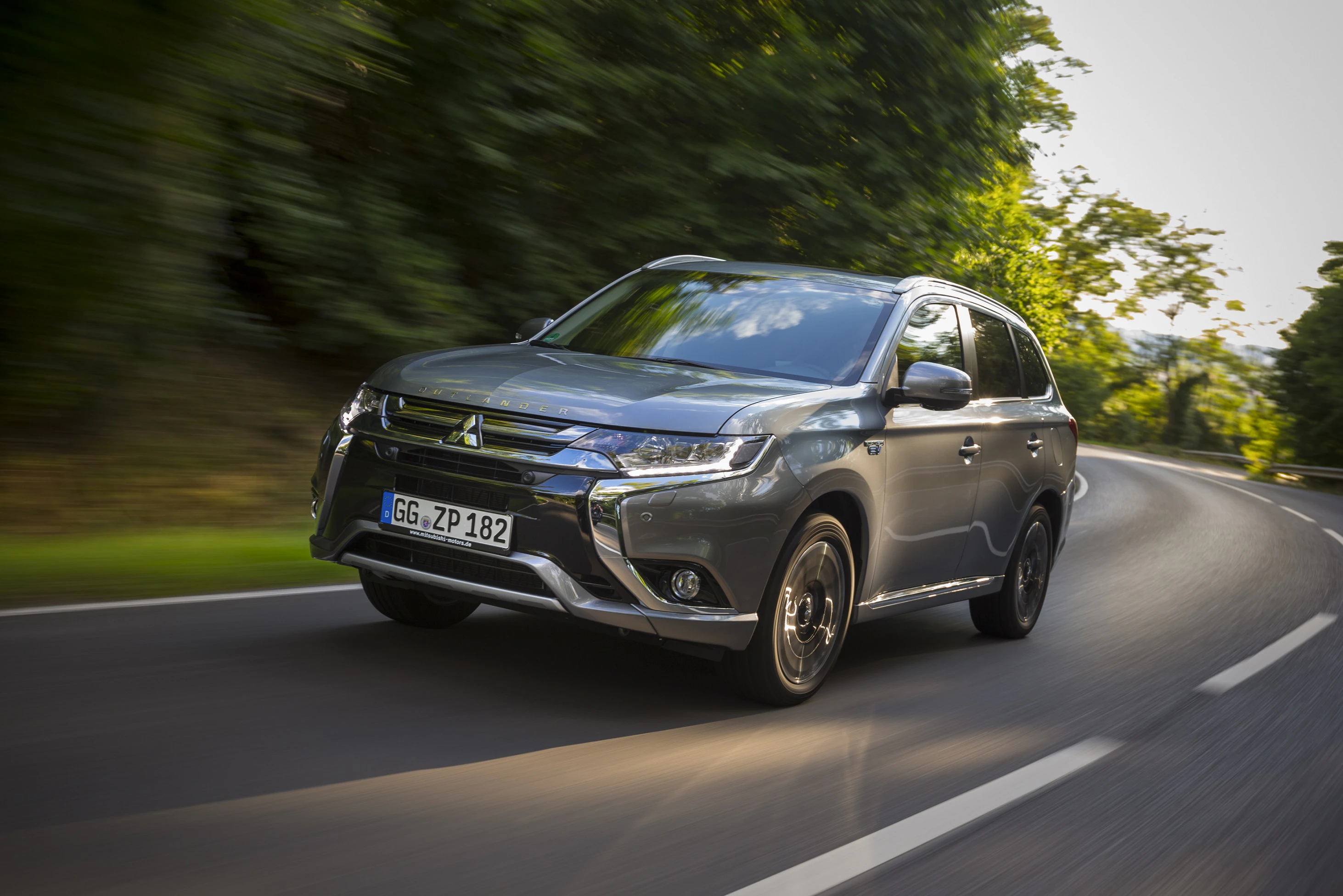 Grauer Mitsubishi SUV fährt auf einer kurvenreichen, von Bäumen gesäumten Straße bei Tageslicht.