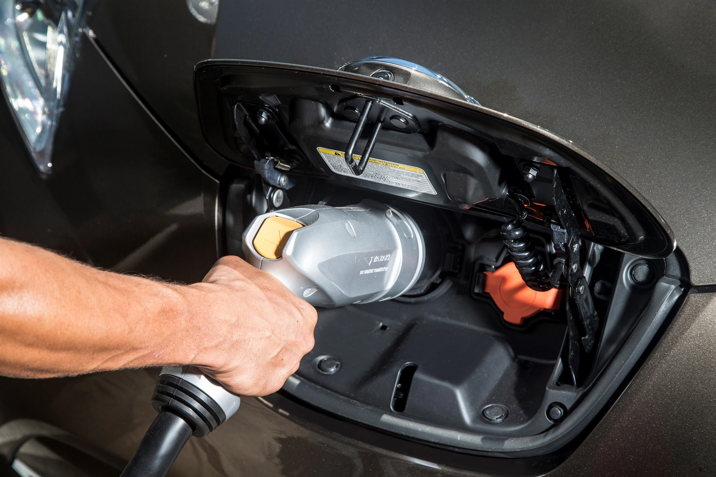 Person lädt ein Elektroauto an einer Ladestation auf. Nahaufnahme der Hand und des Ladesteckers im Anschlussbereich des Fahrzeugs.