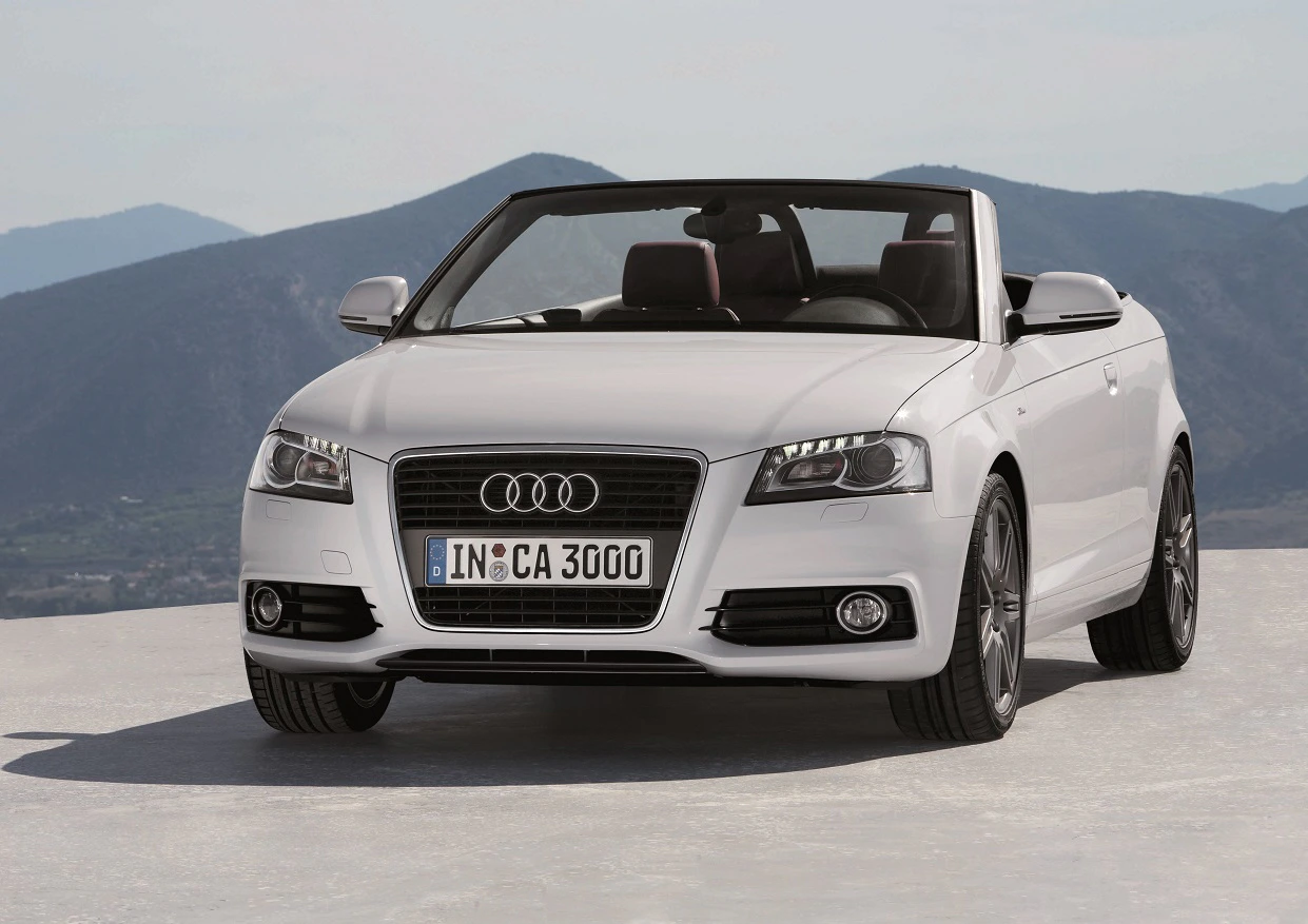 Weißer Audi Cabriolet geparkt auf einem Hügel, mit offenem Verdeck und Berglandschaft im Hintergrund.