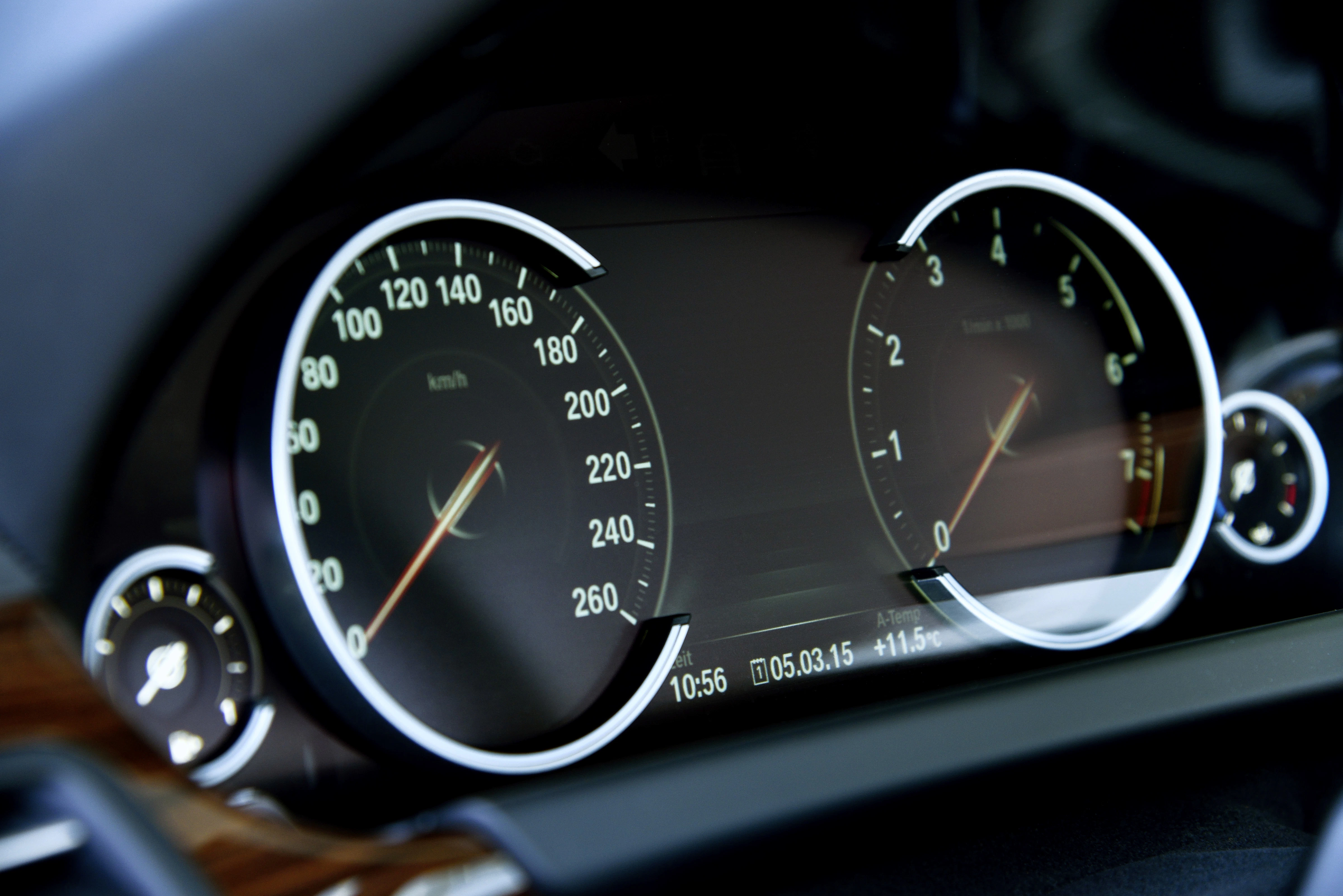 Nahaufnahme eines Autotachos mit Geschwindigkeits- und Drehzahlanzeige, dunkles Armaturenbrett, Uhrzeit und Datum unten sichtbar.