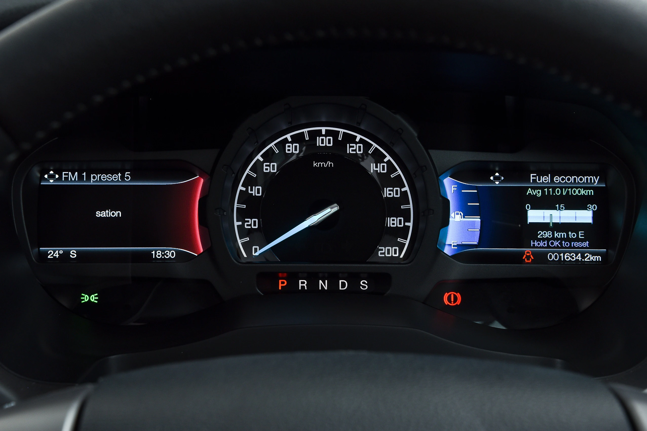 Nahaufnahme eines Auto-Dashboards mit Tachometer in km/h, Ganganzeige, Kraftstoffverbrauch und Radiosender-Anzeige bei 24°C Außentemperatur.