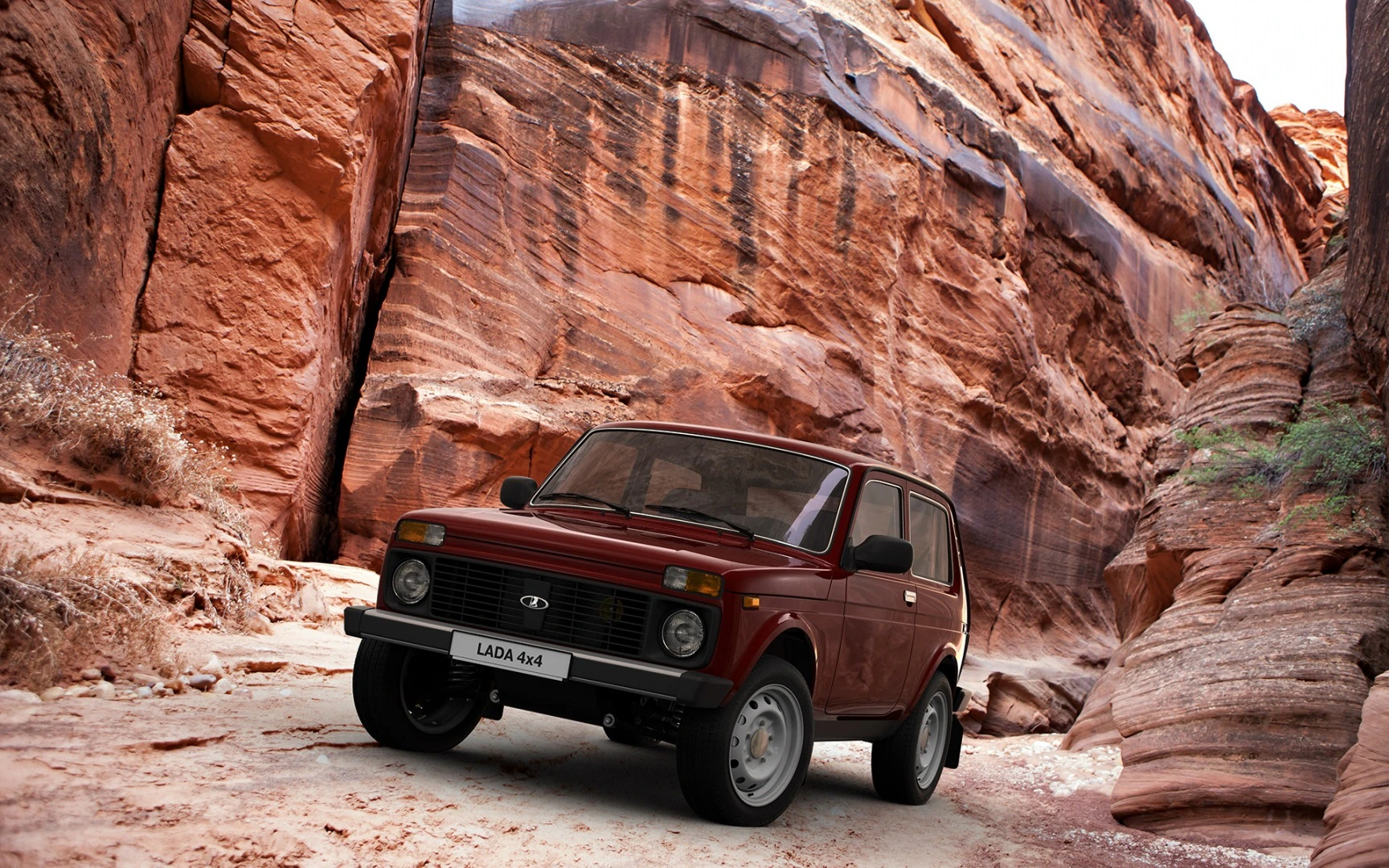 Ein roter Lada 4x4 fährt durch eine enge, felsige Schlucht mit hohen, rotbraunen Felswänden.