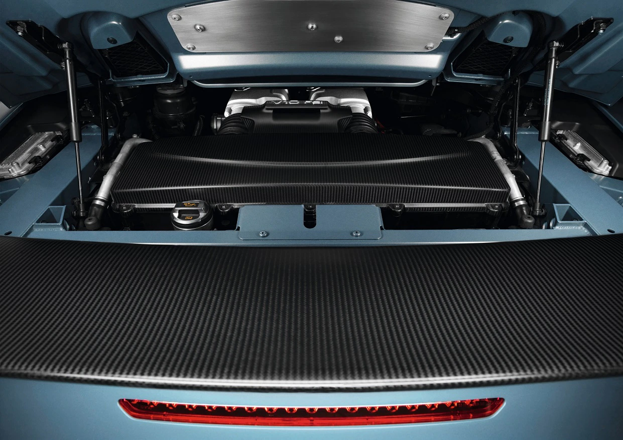 Der Motorraum eines Sportwagens mit offener Motorhaube. Sichtbar ist ein leistungsstarker Motor mit Carbon-Elementen.