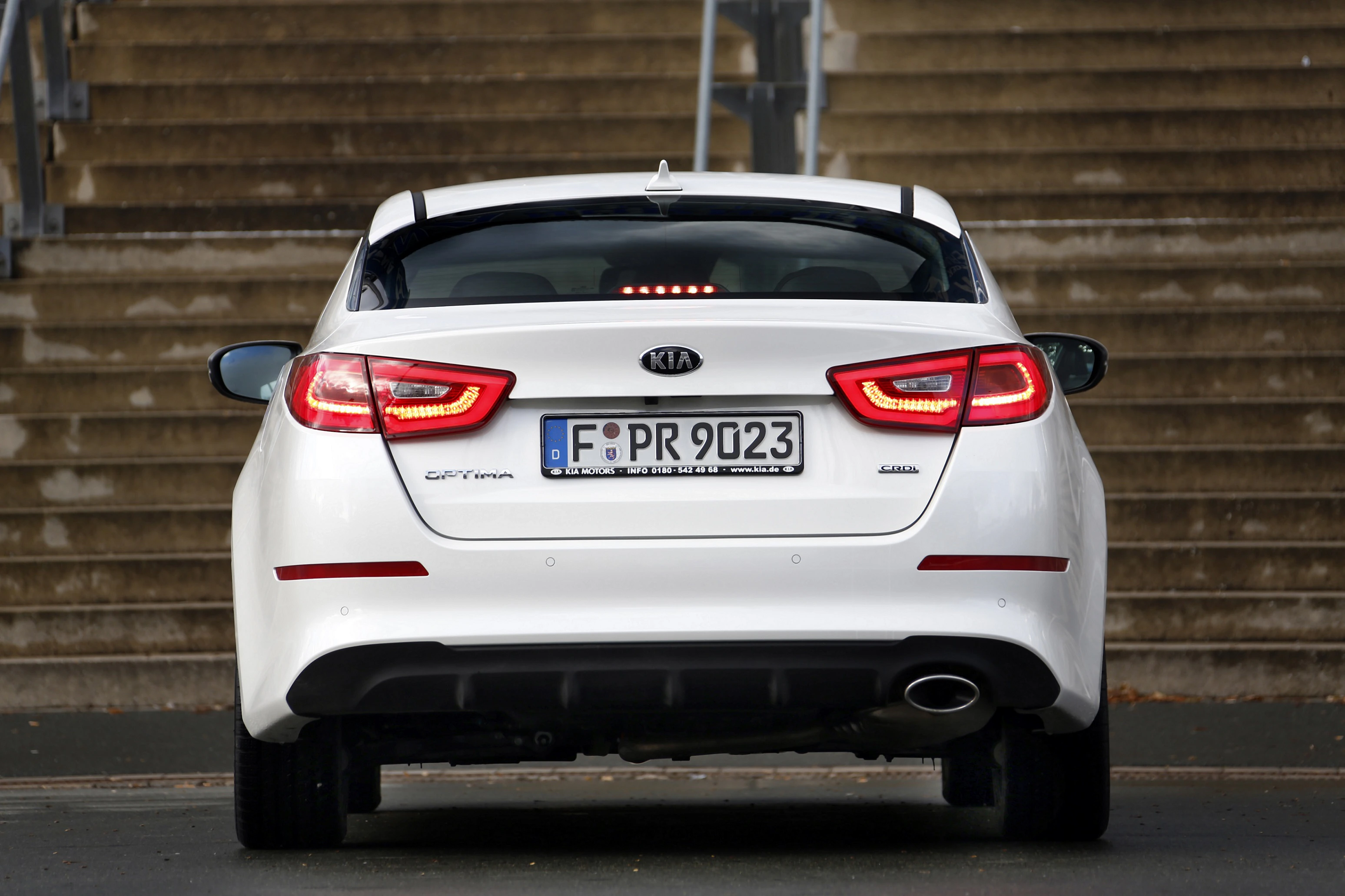 Rückansicht eines weißen Kia Ceed auf einer Straße, im Hintergrund eine Treppe.