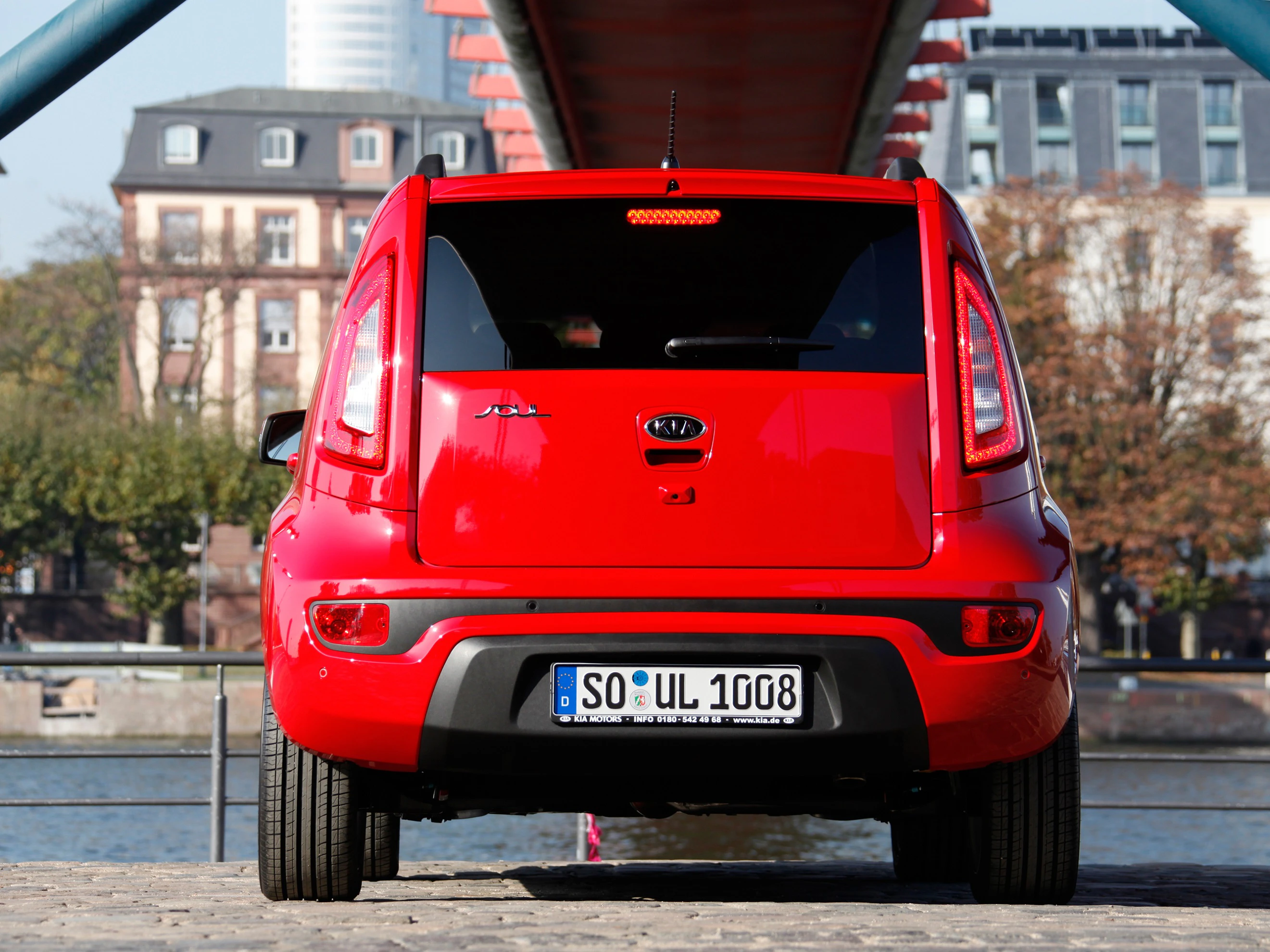 Roter Kia Soul auf Kopfsteinpflaster vor einer Backsteinbrücke. Im Hintergrund sind Bäume und Gebäude zu sehen.