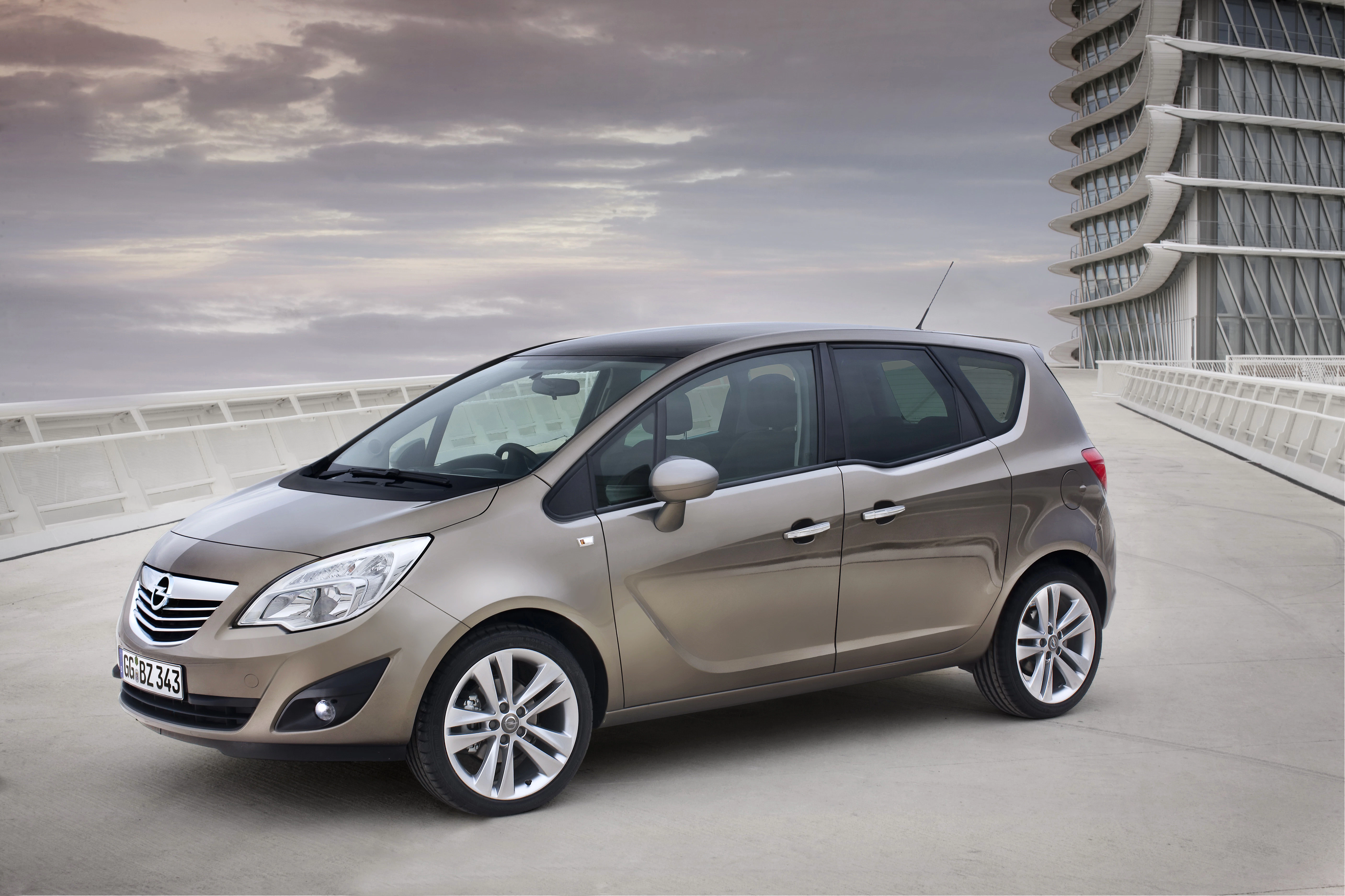 Brauner Opel Meriva steht auf einer Brücke vor moderner Architektur, bewölkter Himmel im Hintergrund.