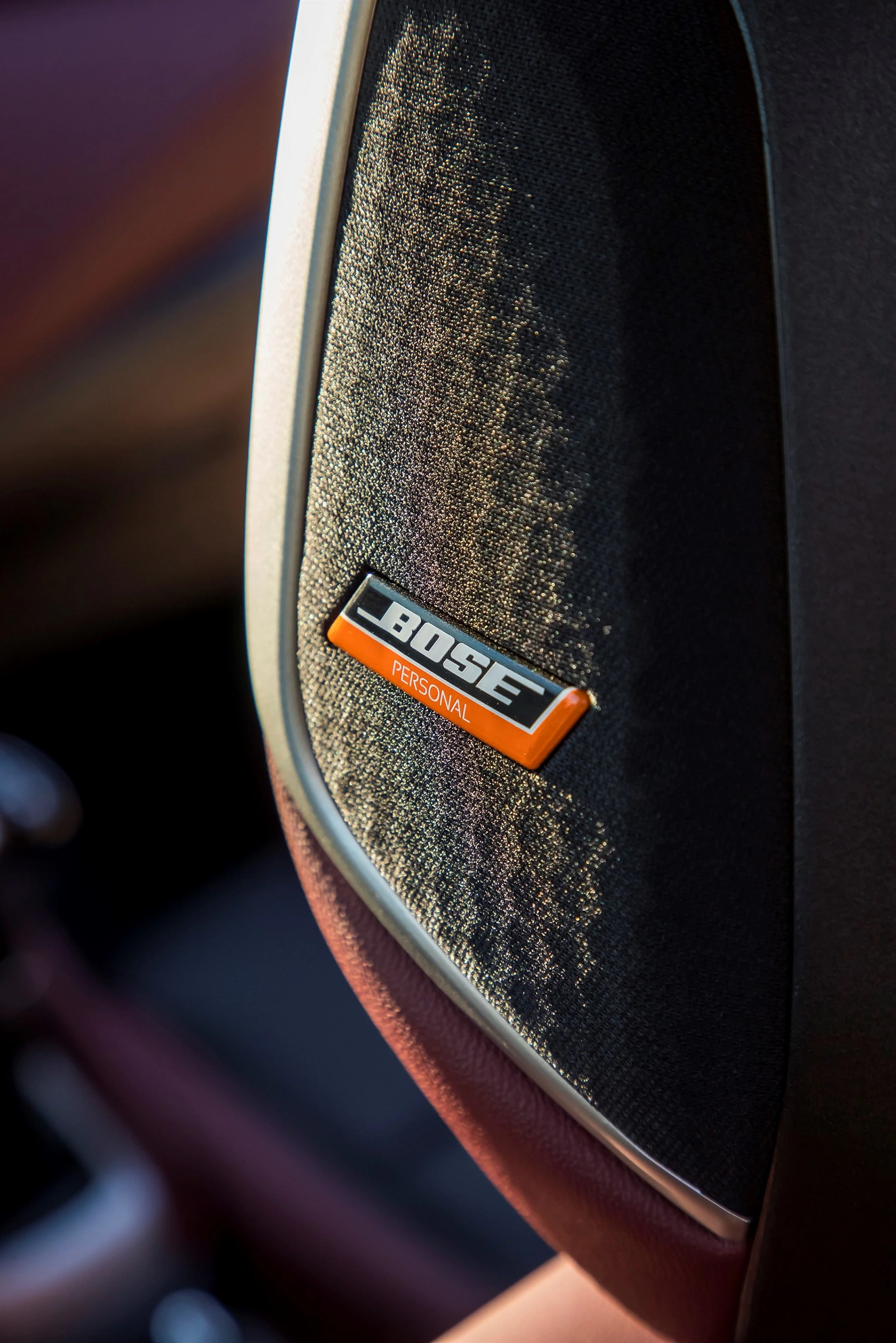 Nahaufnahme eines Autositzes mit einem schwarzen Stoffbezug und einem orangefarbenen "Bose Personal"-Logo.