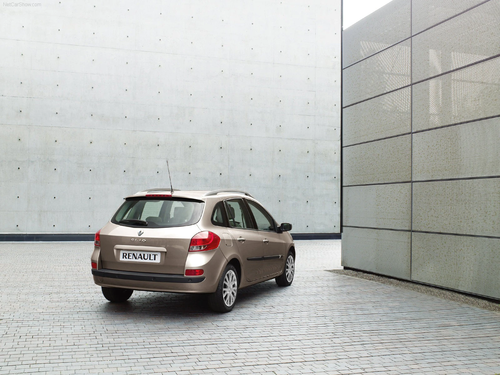 Silberner Renault Kleinwagen parkt auf einem modernen, gepflasterten Hof zwischen zwei grauen Gebäudewänden bei Tageslicht.