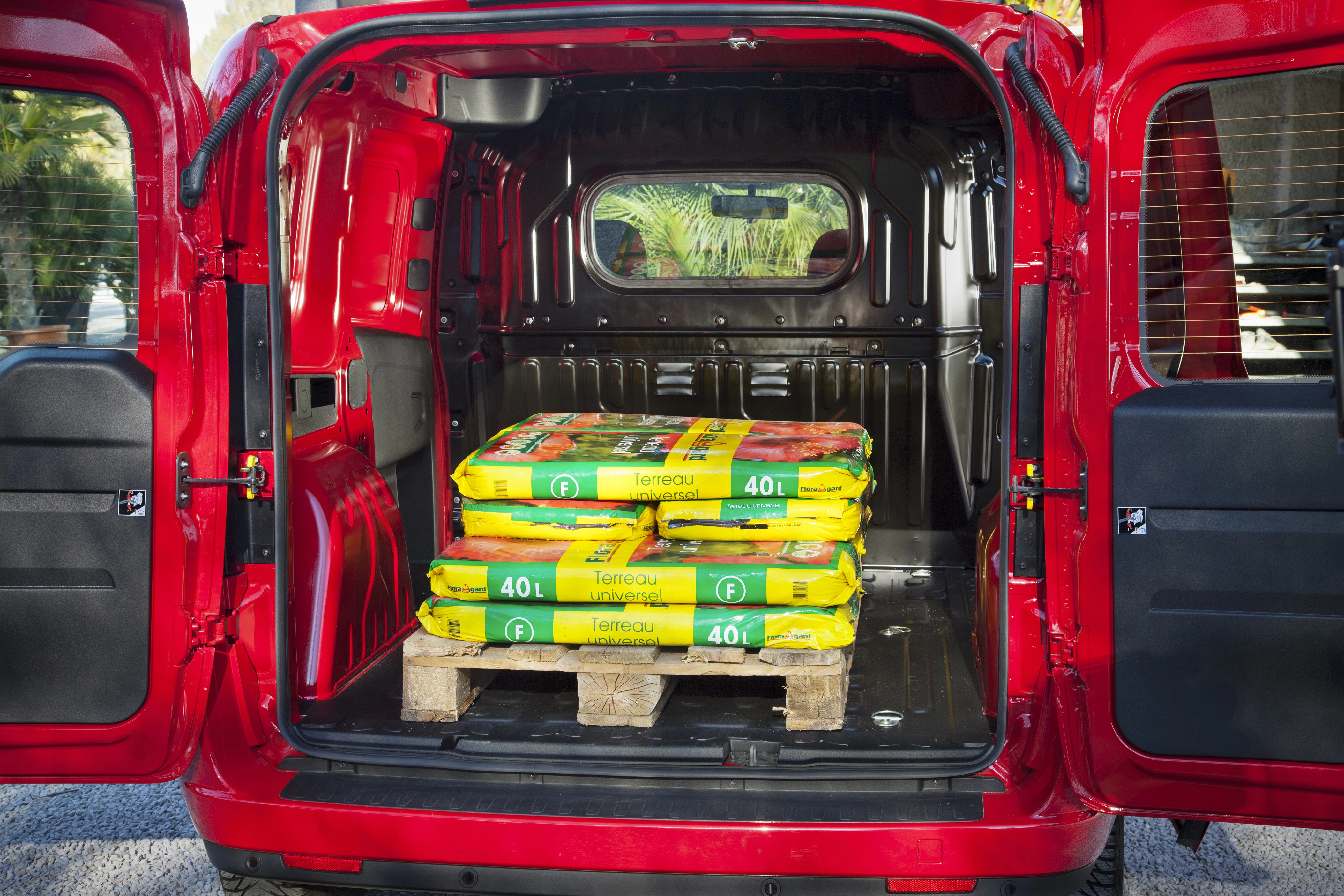 Roter Transporter mit offener Heckklappe, beladen mit Paletten mit gelben Säcken Blumenerde.