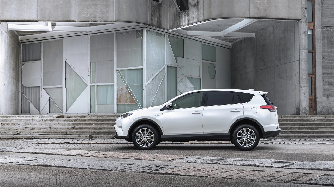 Weißer SUV vor modernem, geometrisch gestaltetem Gebäude mit grauen Betonwänden und großen, dekorativen Fenstern.