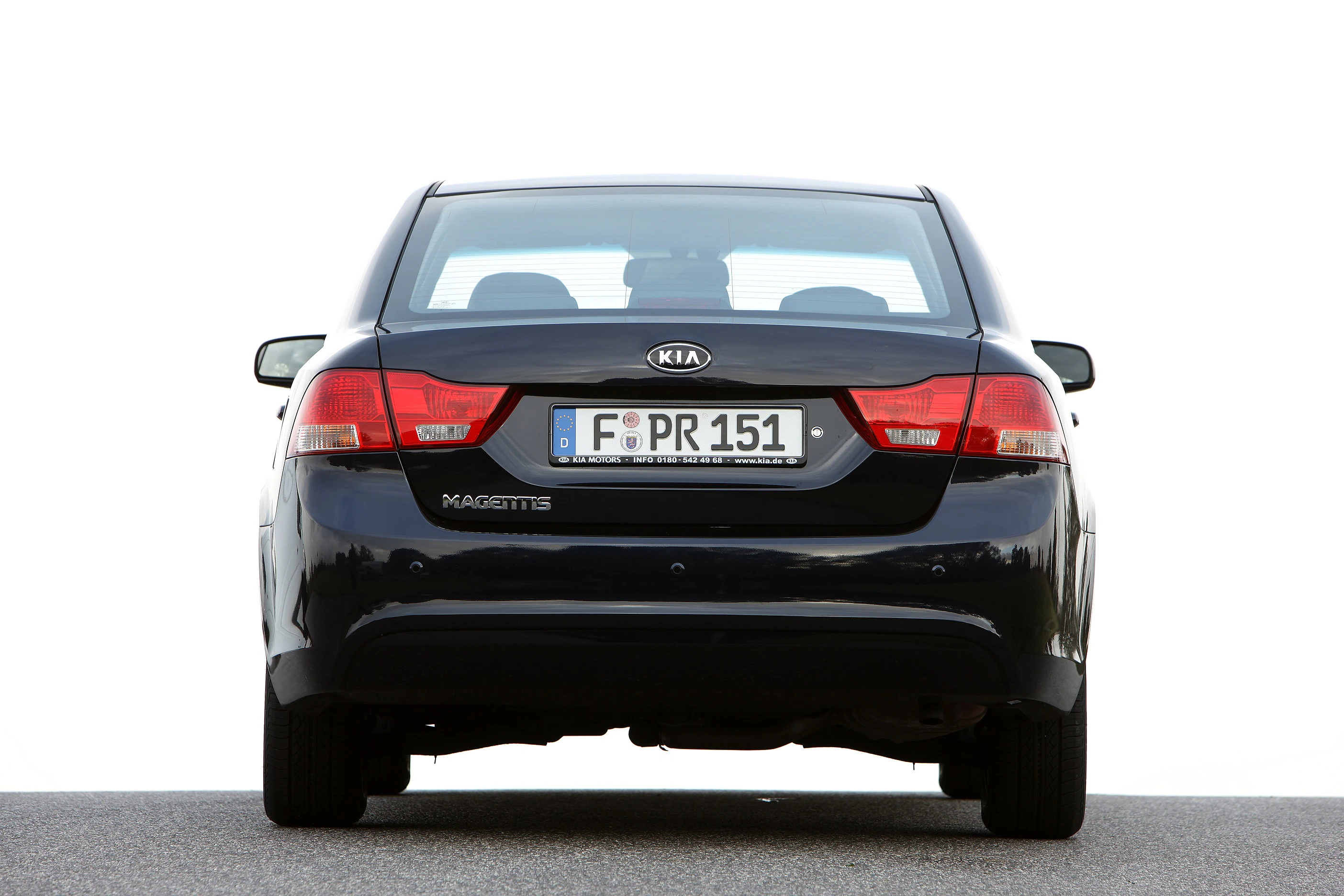 KIA Magentis in Schwarz, von hinten fotografiert, auf einer grauen Straße. Europäisches Kennzeichen sichtbar. Freier, weißer Hintergrund.
