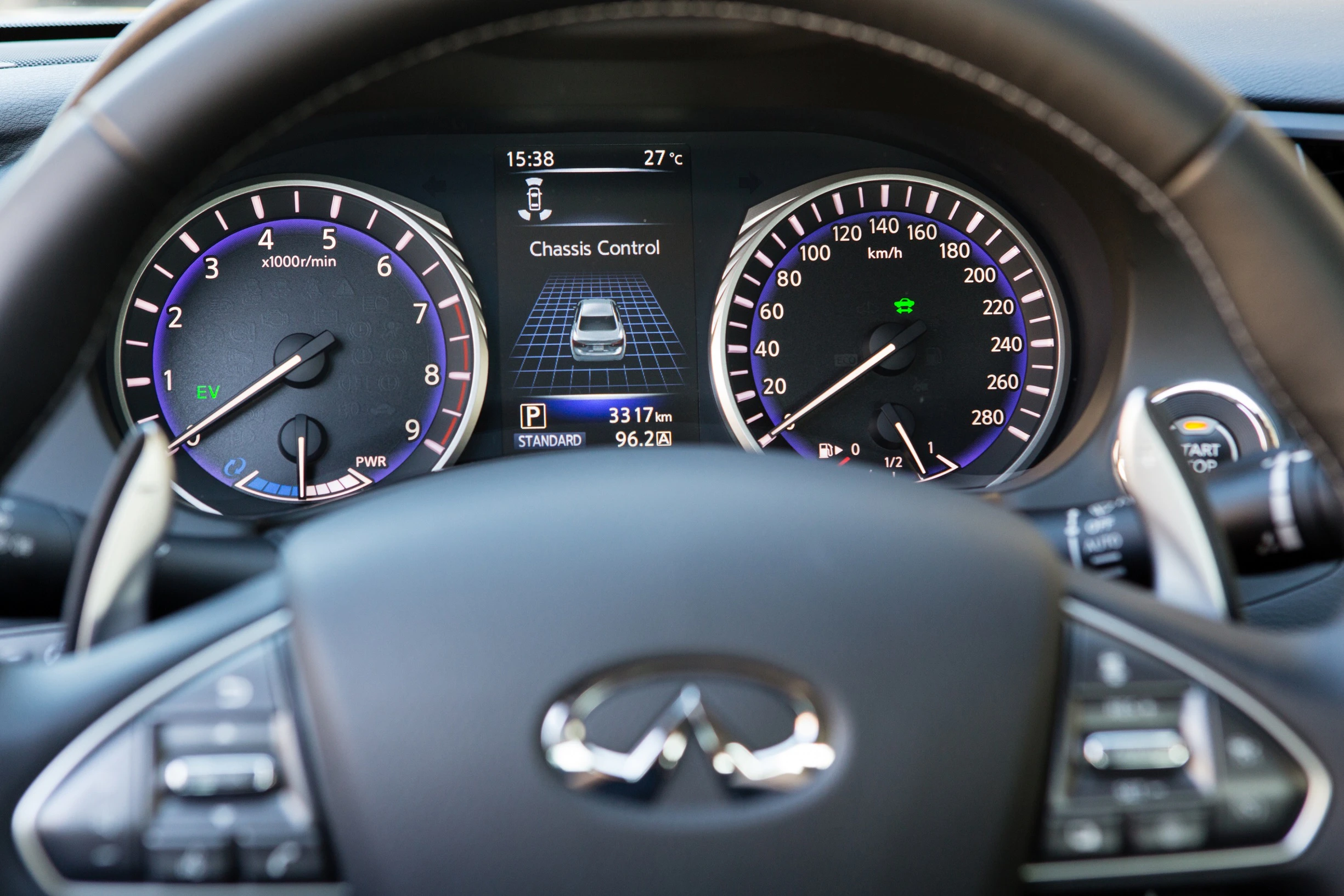 Nahaufnahme eines Autotachos mit digitalen Anzeigen: Geschwindigkeit, Kilometerstand und Temperatur bei 27°C. Lenkrad im Vordergrund.